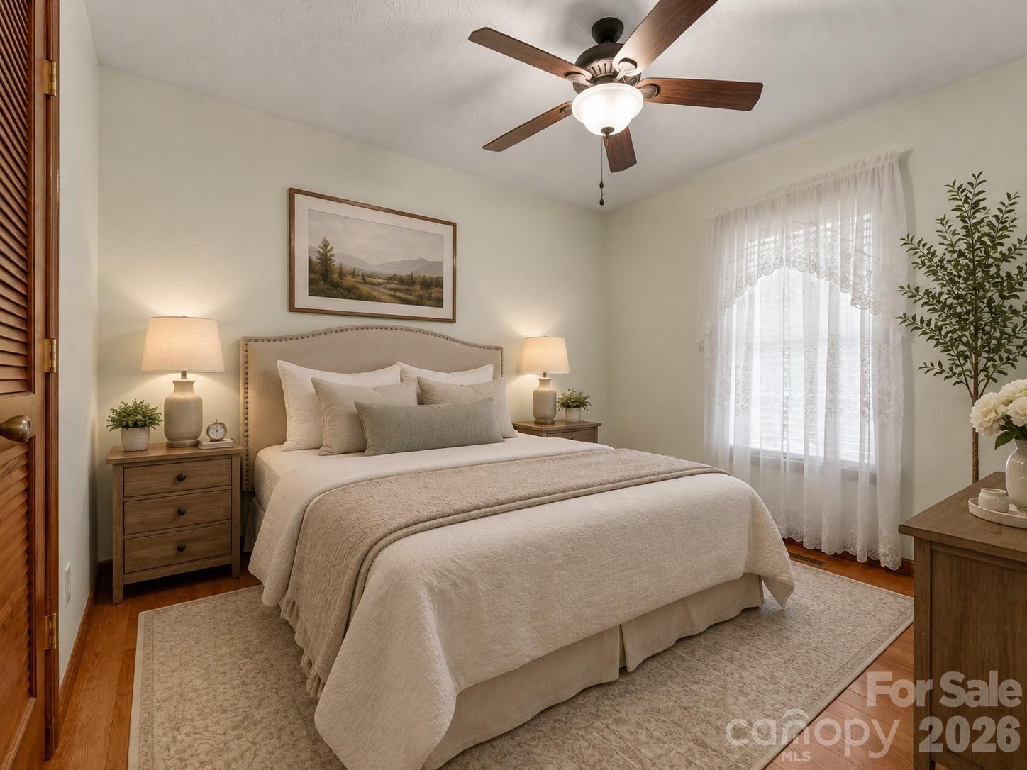 Bedroom with a neatly made bed, wood nightstands, ceiling fan, and lace curtains.