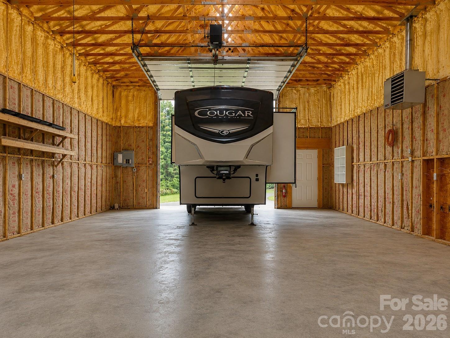 Unfinished garage with a Cougar fifth-wheel RV parked beneath an open overhead door.