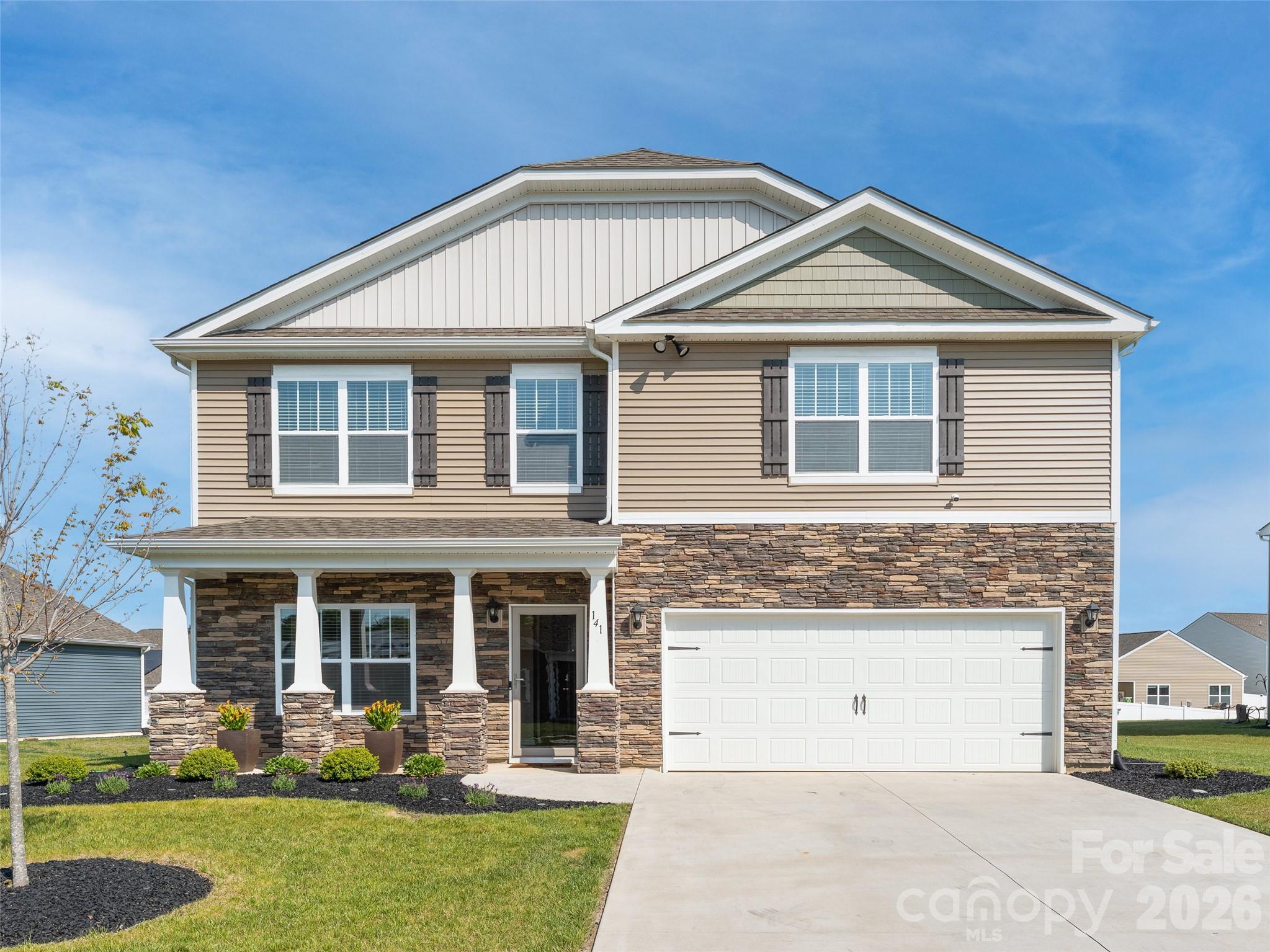 Two-story beige house with stone veneer, covered porch, and double garage at 141.