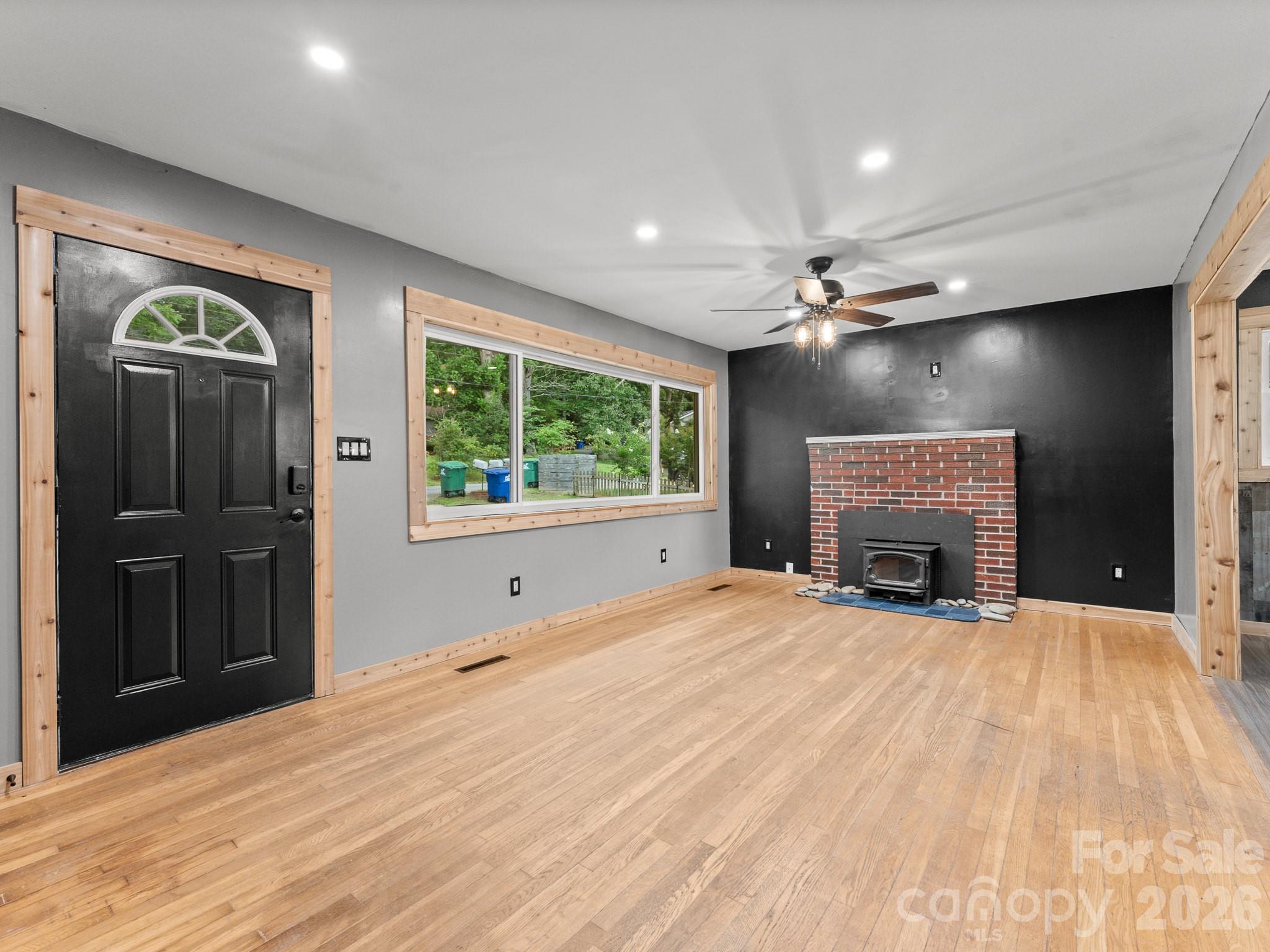 Living room with hardwood floors, a brick fireplace and wood stove, black accent wall, and natural wood trim.
