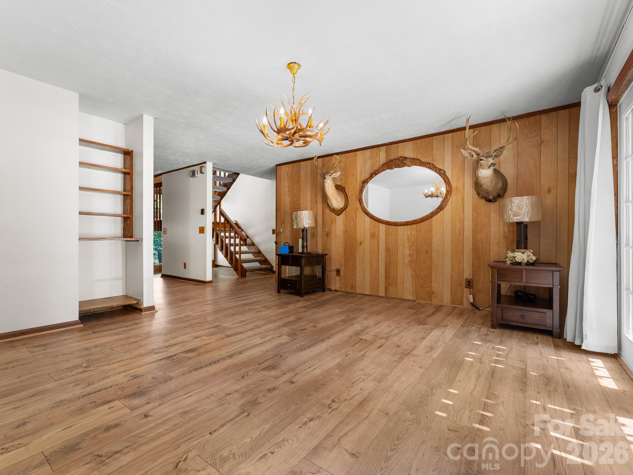 Living room with wood flooring, paneled wall, deer mounts, and a staircase.