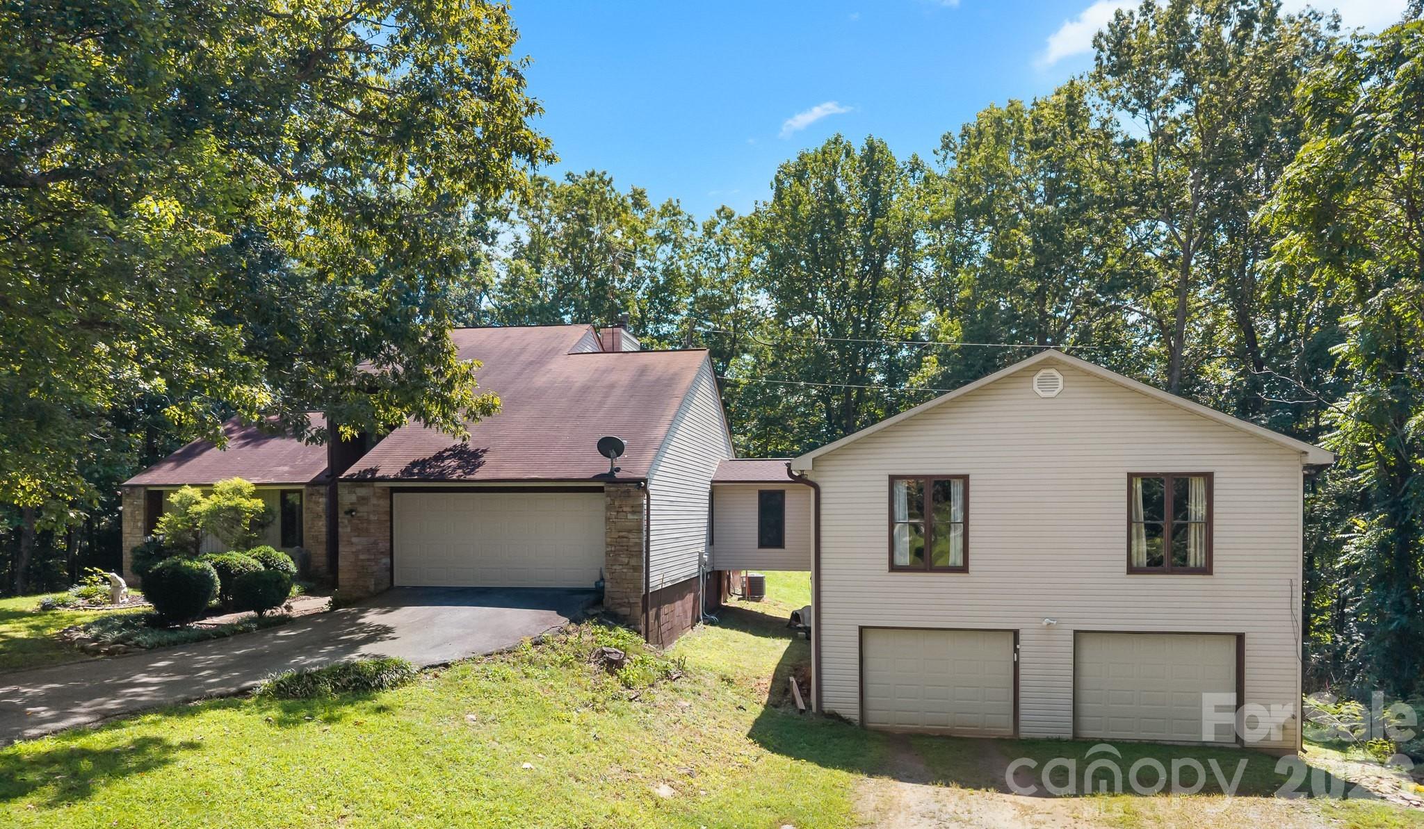 Wooded home with stone-and-siding exterior and multiple garage doors.