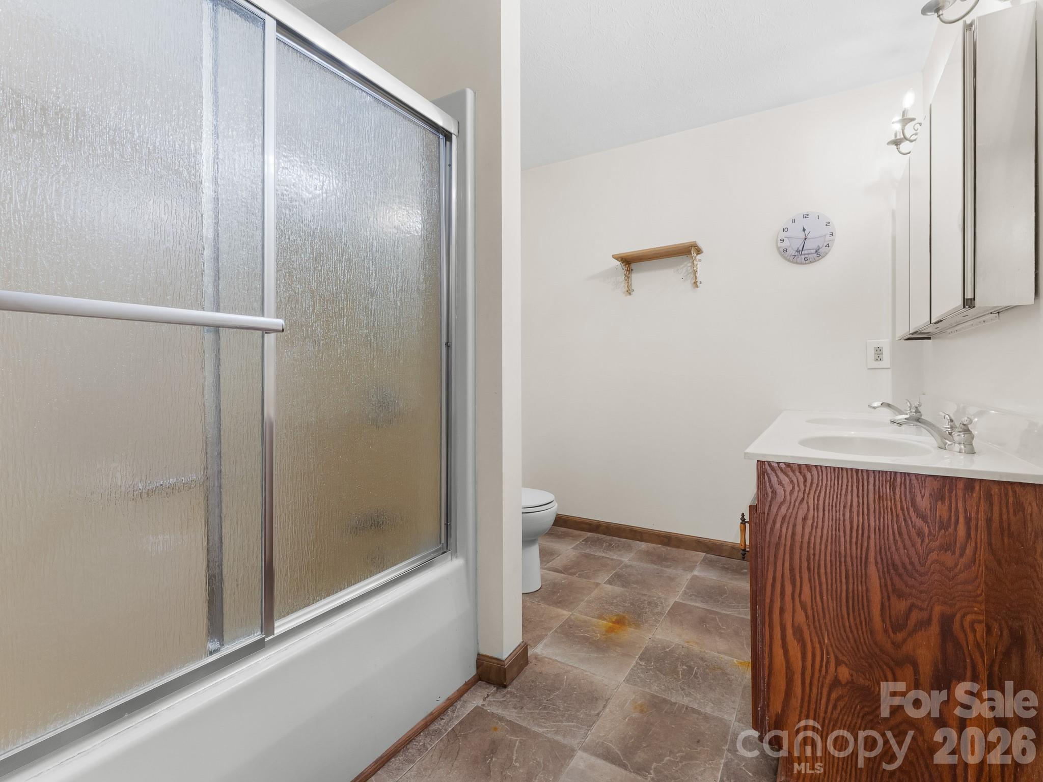 Bathroom with frosted-glass shower, toilet, and double-sink wood vanity.