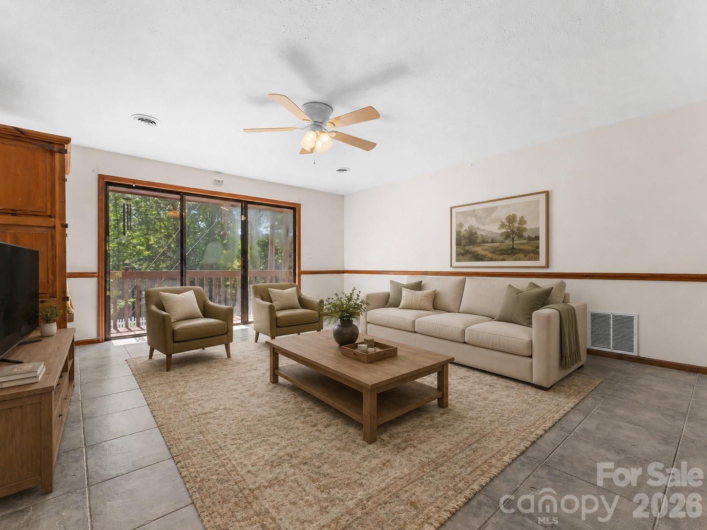 Living room with beige seating, a wooden coffee table, and sliding glass doors overlooking greenery.