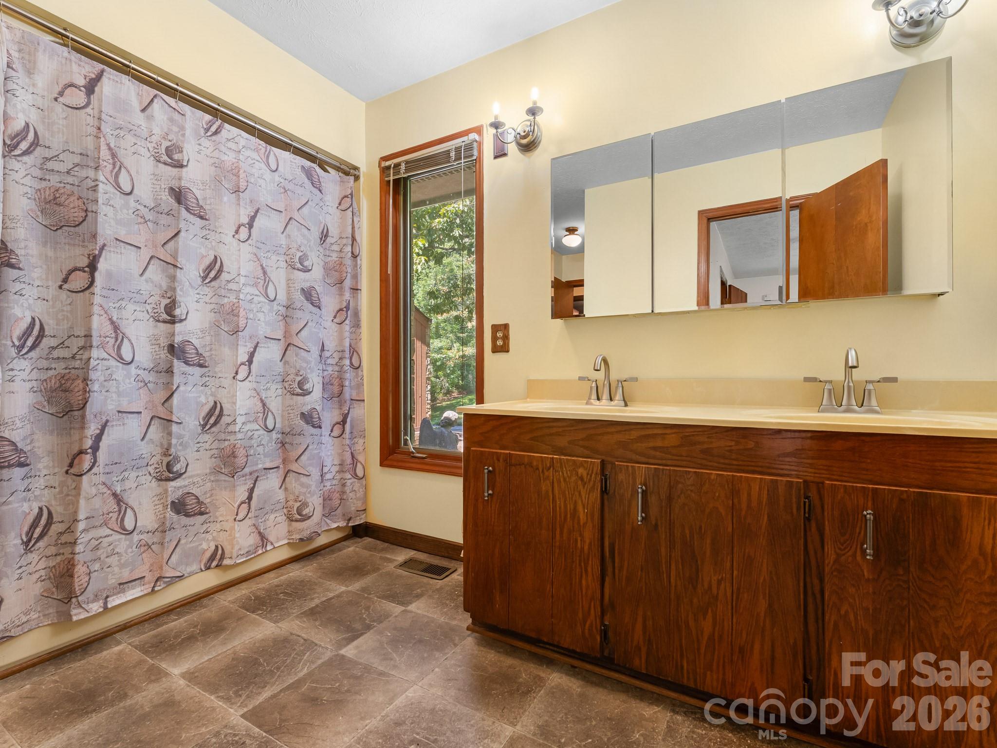 Bathroom with a double-sink wood vanity, mirrored cabinet, and seashell-patterned shower curtain.