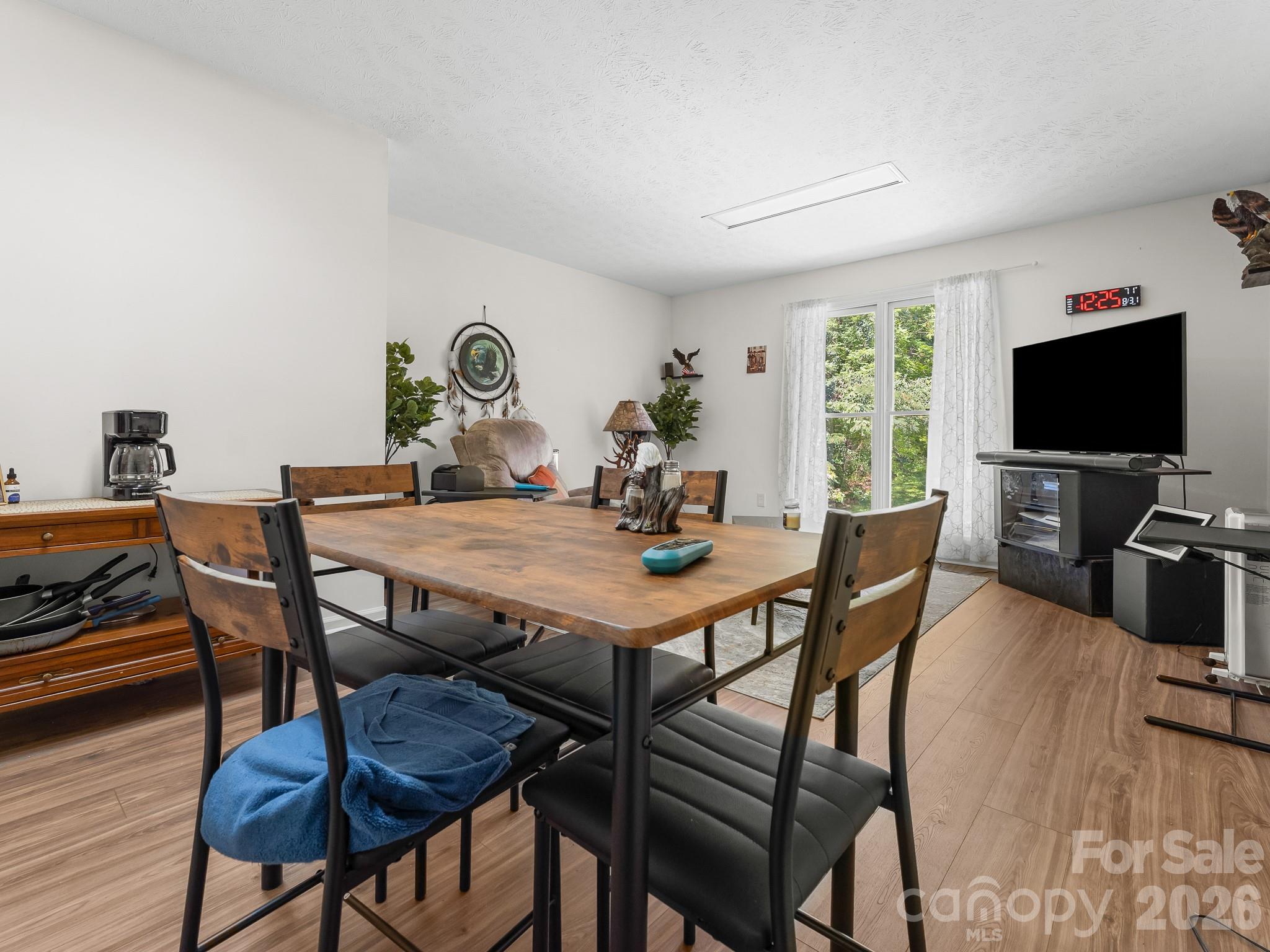 Dining area with a large wooden table, black-cushioned chairs, and a bright window beside the living area.
