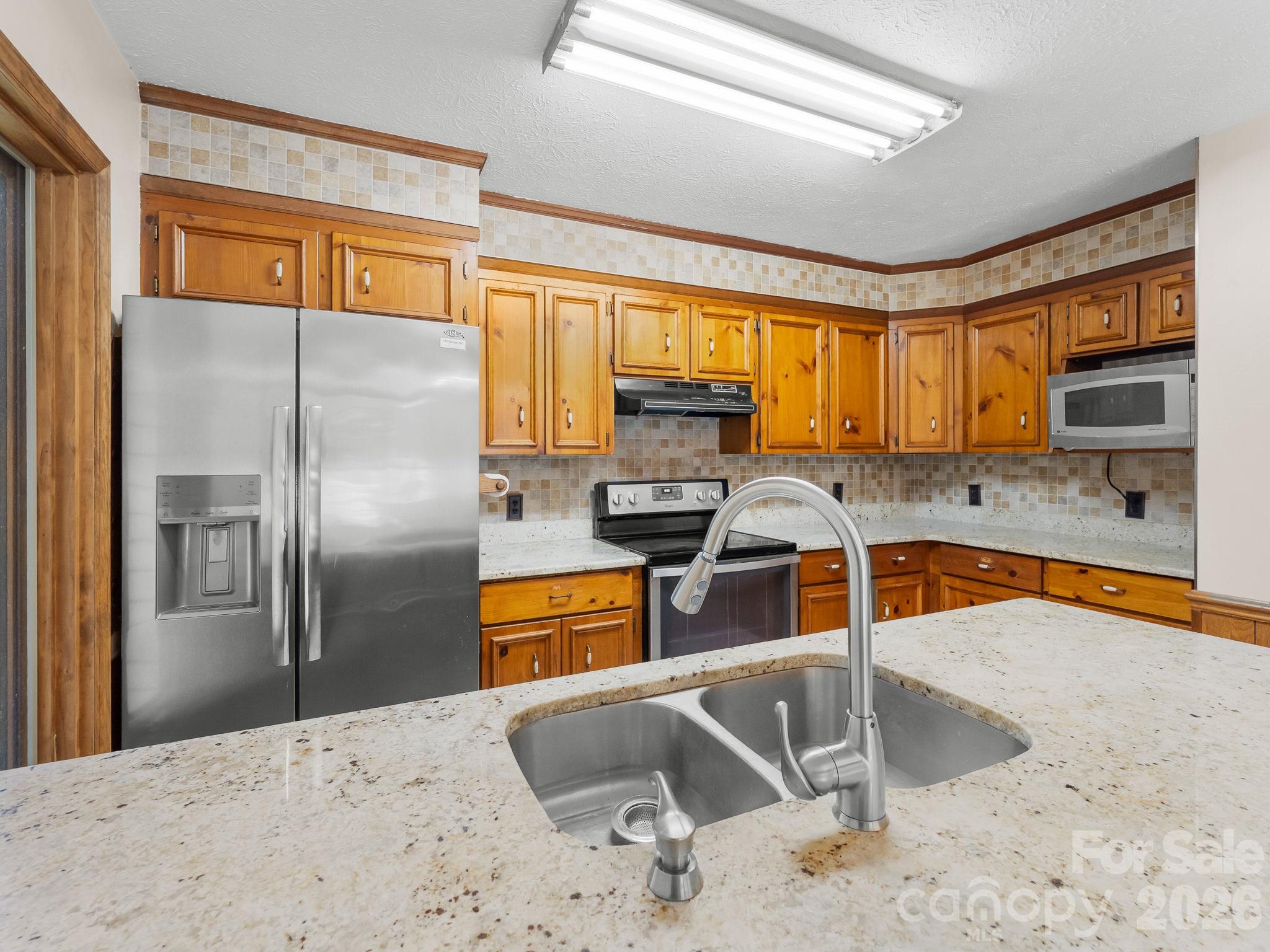 Kitchen with honey-colored cabinets, stainless steel appliances, and a foreground double-basin sink.