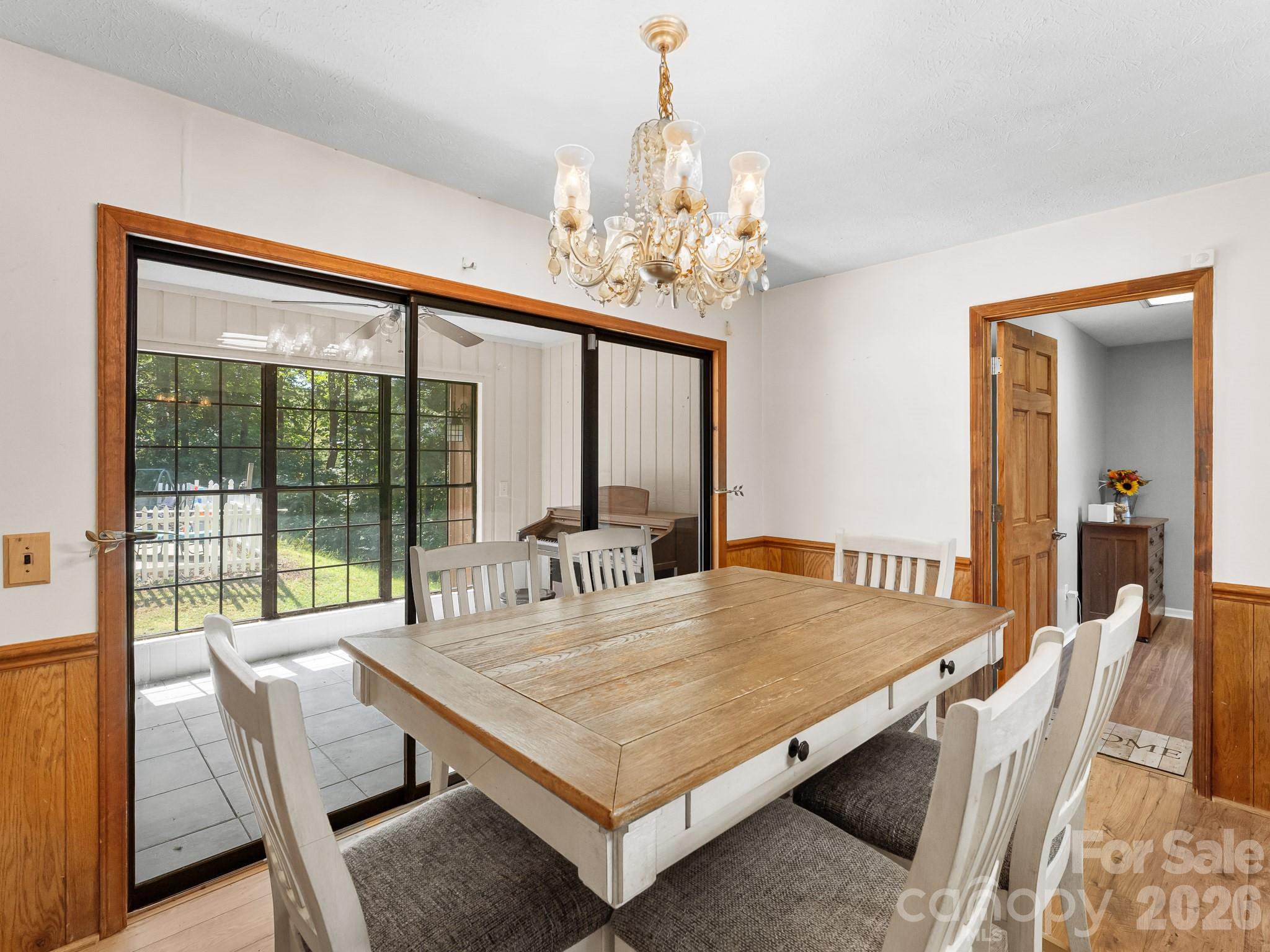 Dining room with a rustic wood table, chandelier, and sliding glass doors to a sunroom.