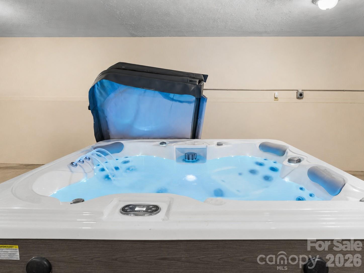 White indoor hot tub with blue-lit water, multiple jets, and its cover raised.