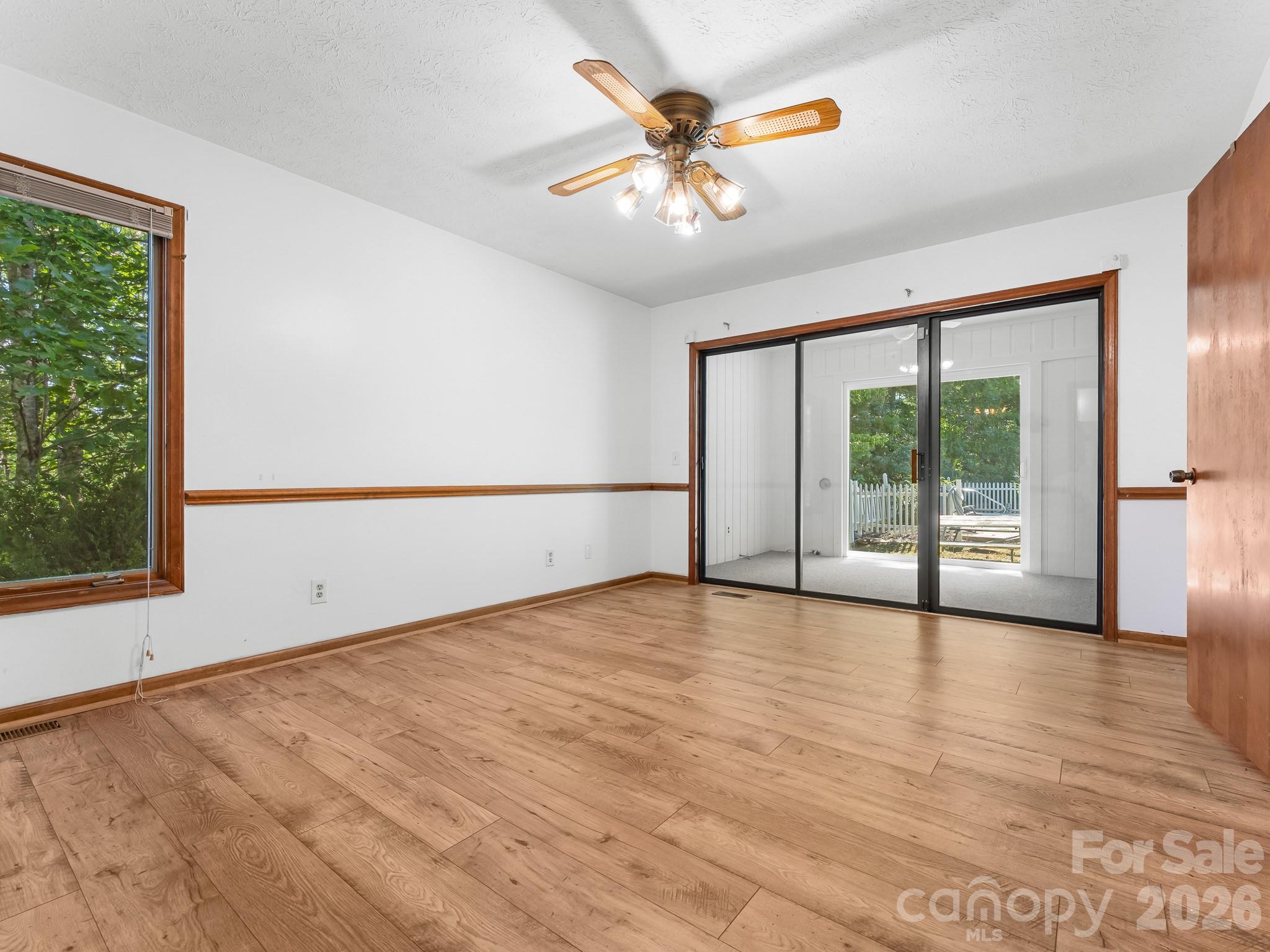 Empty room with wood flooring, a ceiling fan, and sliding glass doors to an enclosed porch.