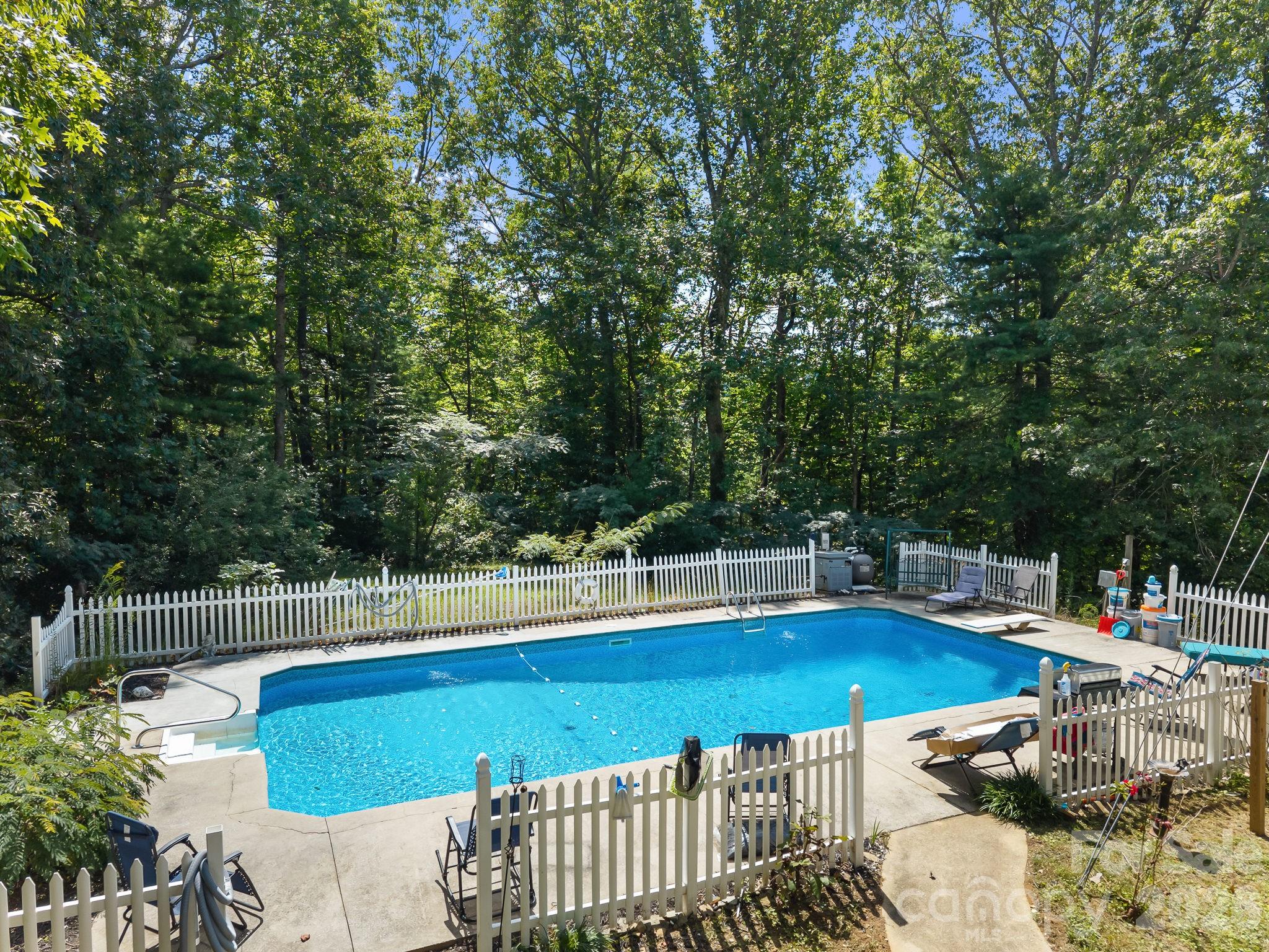 Outdoor swimming pool with white picket fencing, patio loungers, and a wooded backdrop.