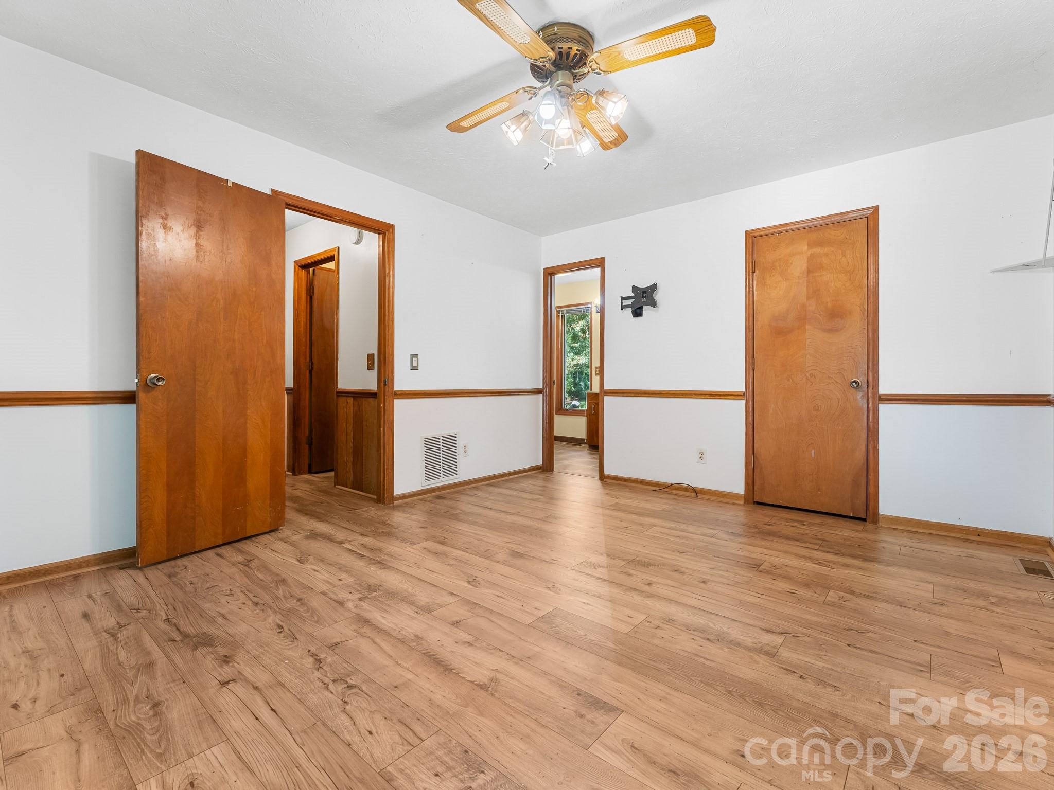 Vacant room with wood-look flooring, wood trim, several doorways, and a ceiling fan.
