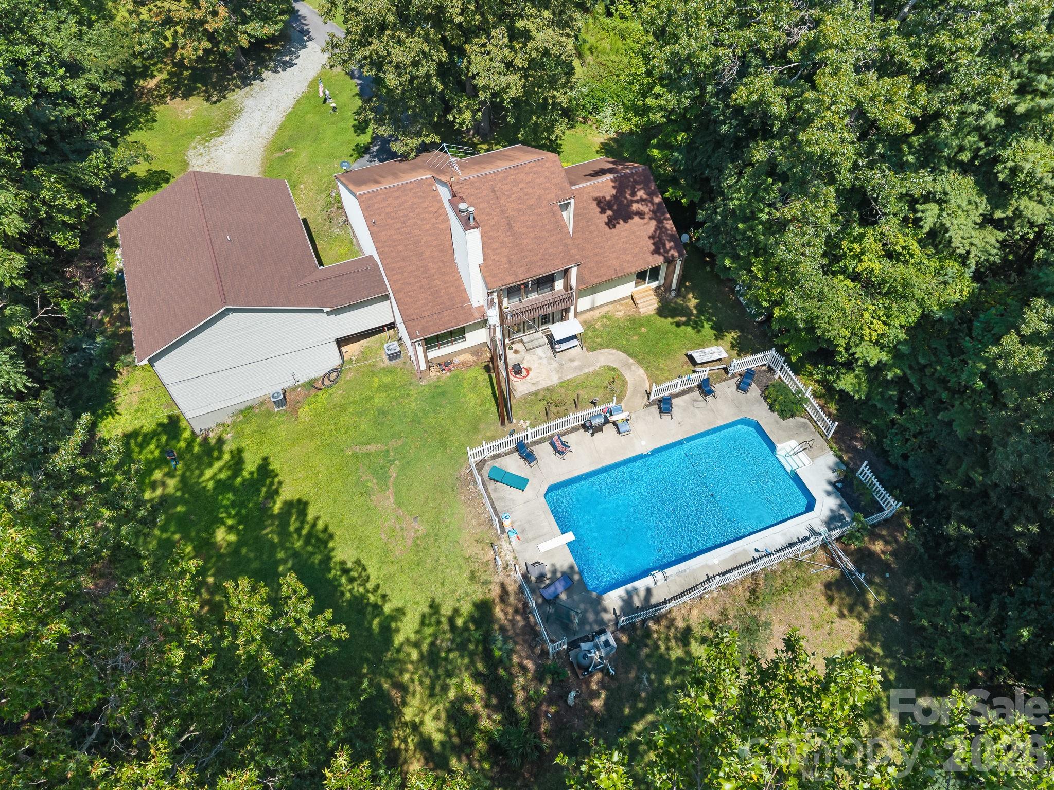 Aerial view of a wooded home with a fenced pool and detached garage.