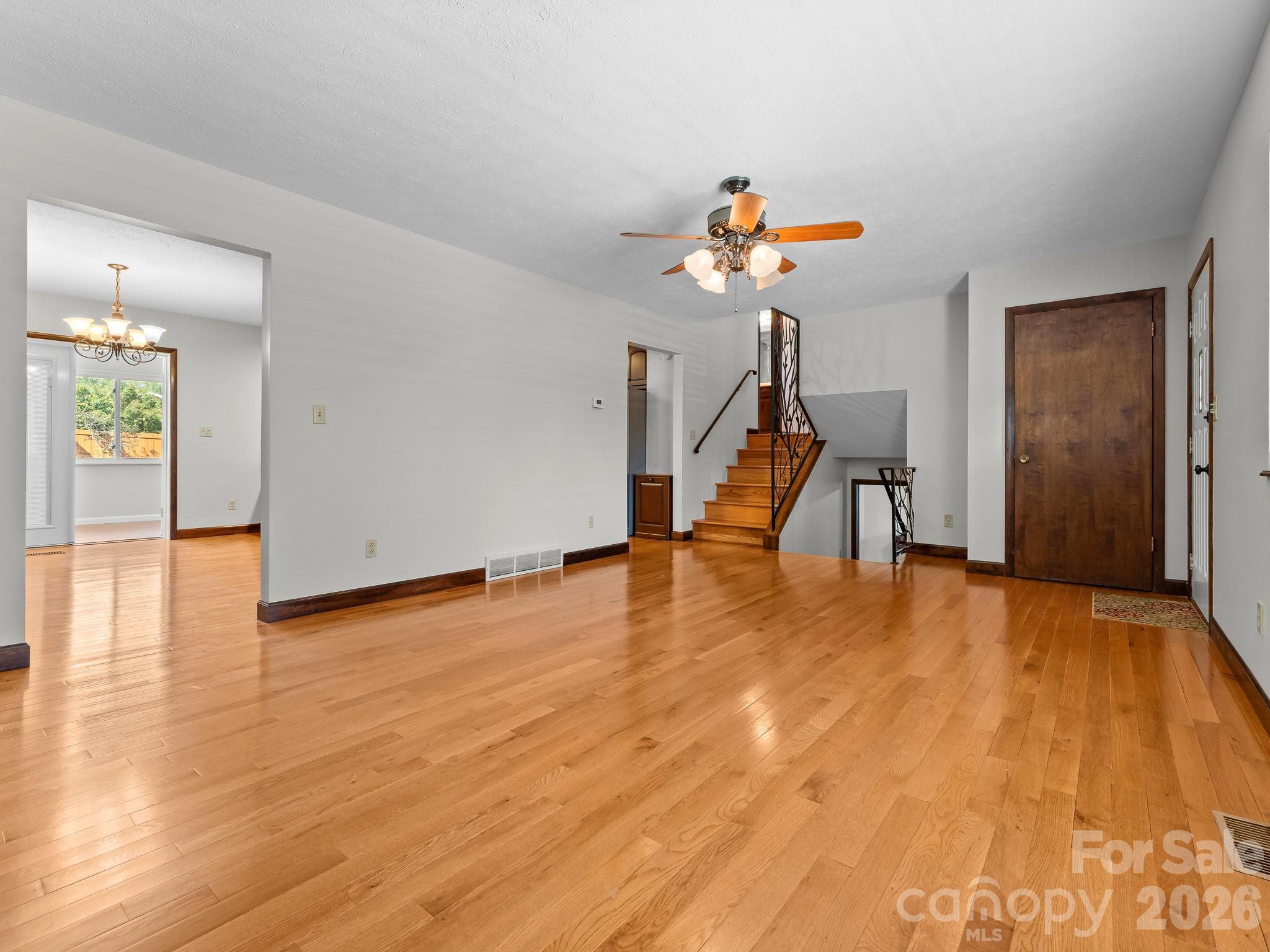 Empty living room with polished hardwood floors, a wooden staircase, and a ceiling fan.