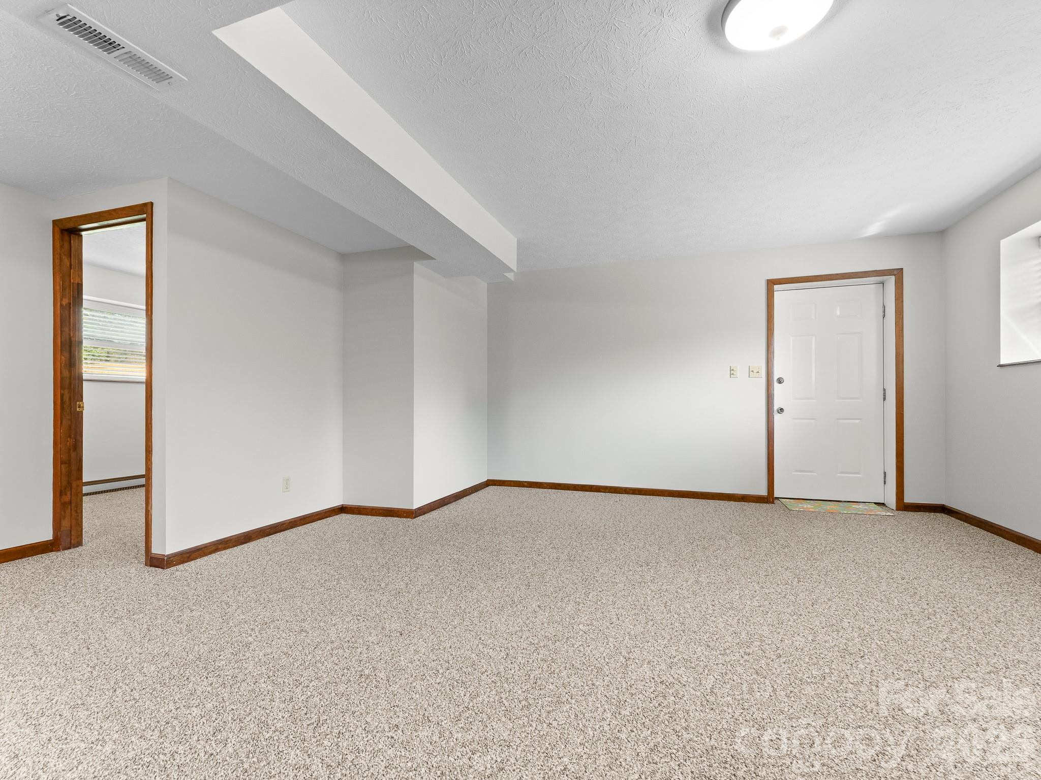 Empty carpeted room with wood trim, a front door, and an open doorway to another room.