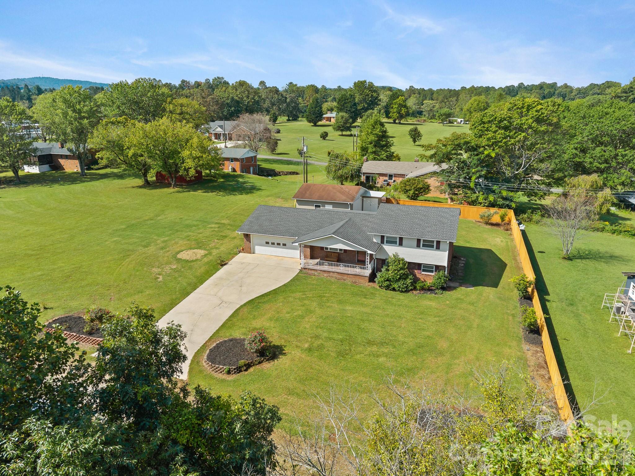 Aerial view of a split-level home with a broad lawn, attached garage, driveway, and fenced backyard.
