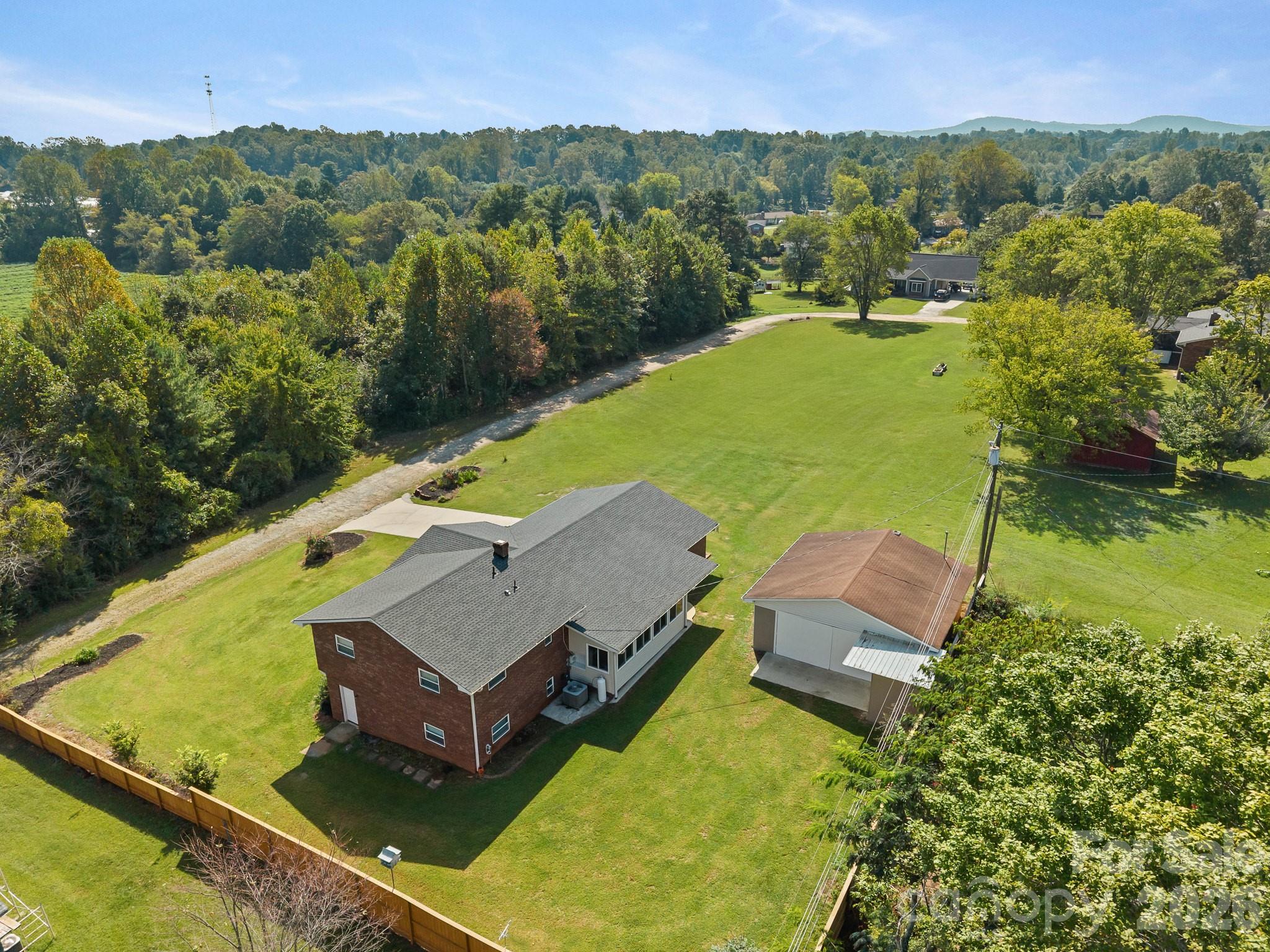 Aerial view of a brick house with a detached garage, fenced lawn, and distant mountain ridges.
