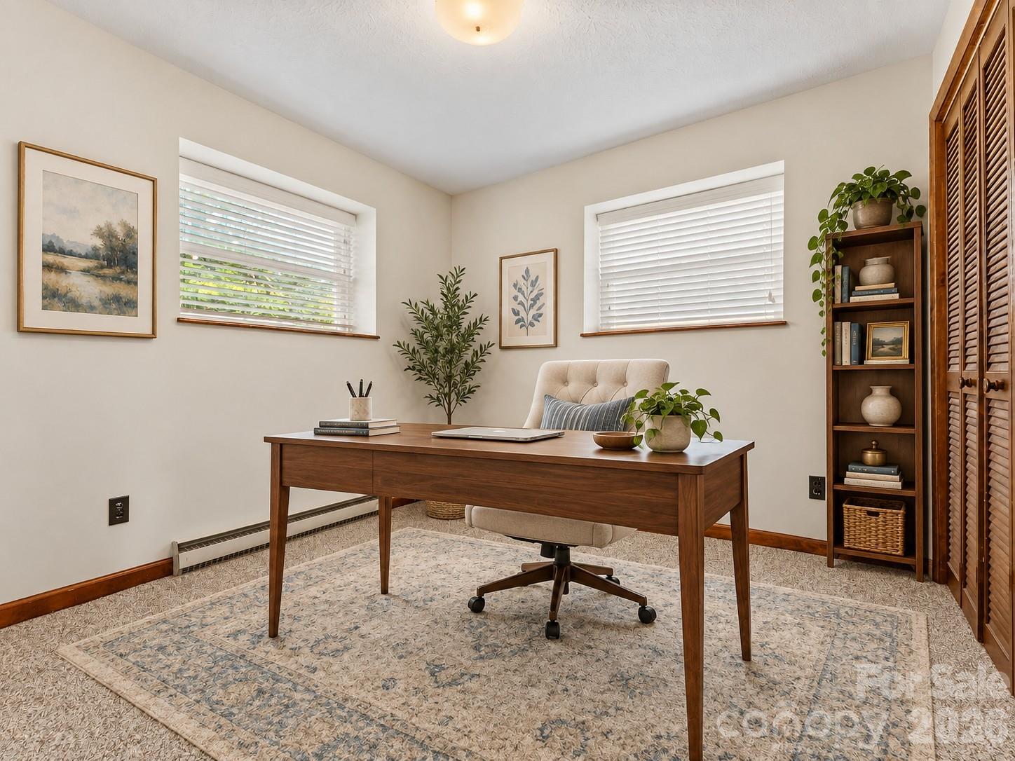 Furnished home office with a dark wood desk, cream chair, patterned rug, and tall bookcase.