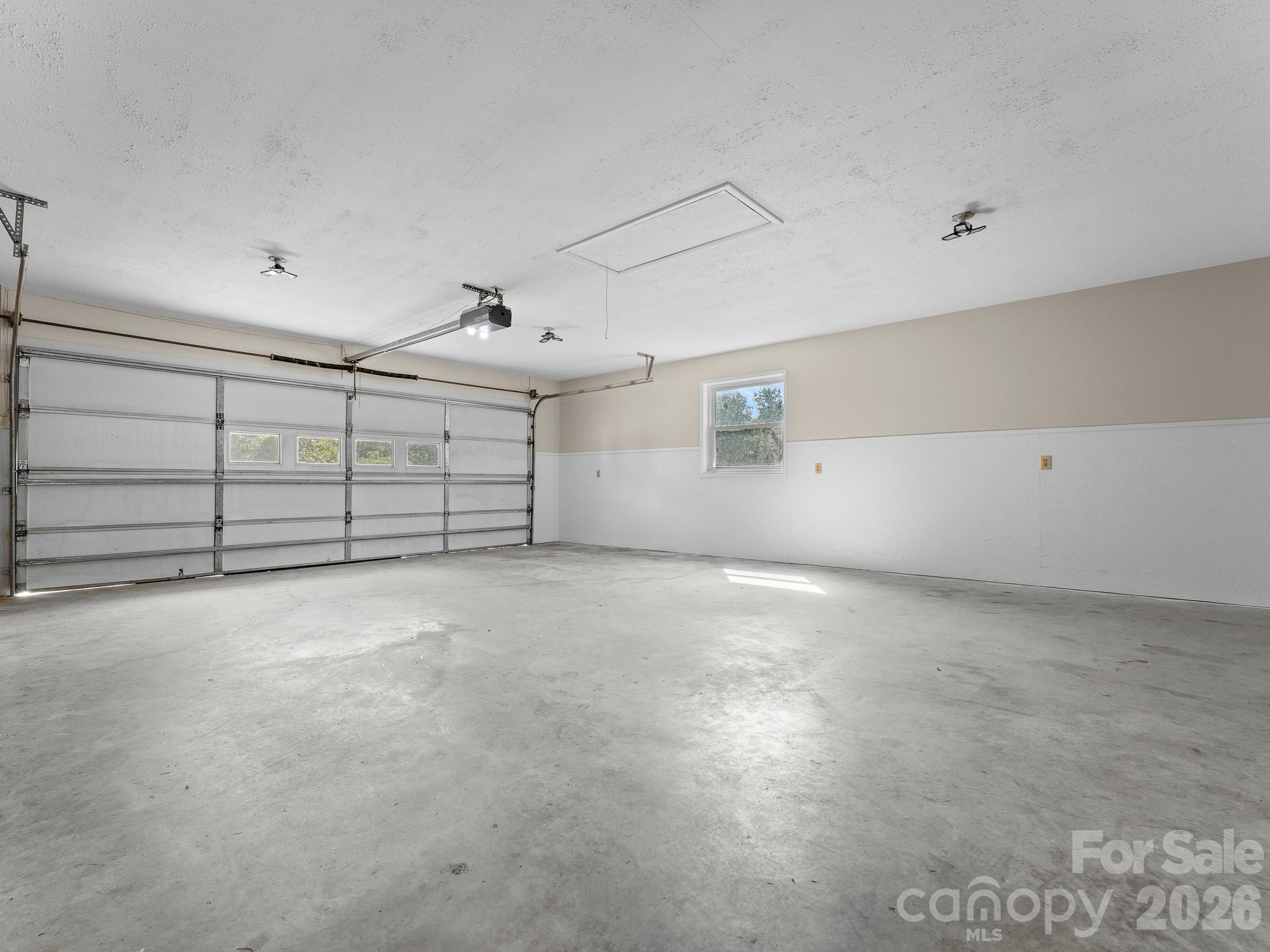 Empty garage with a wide sectional door and window on the side wall.