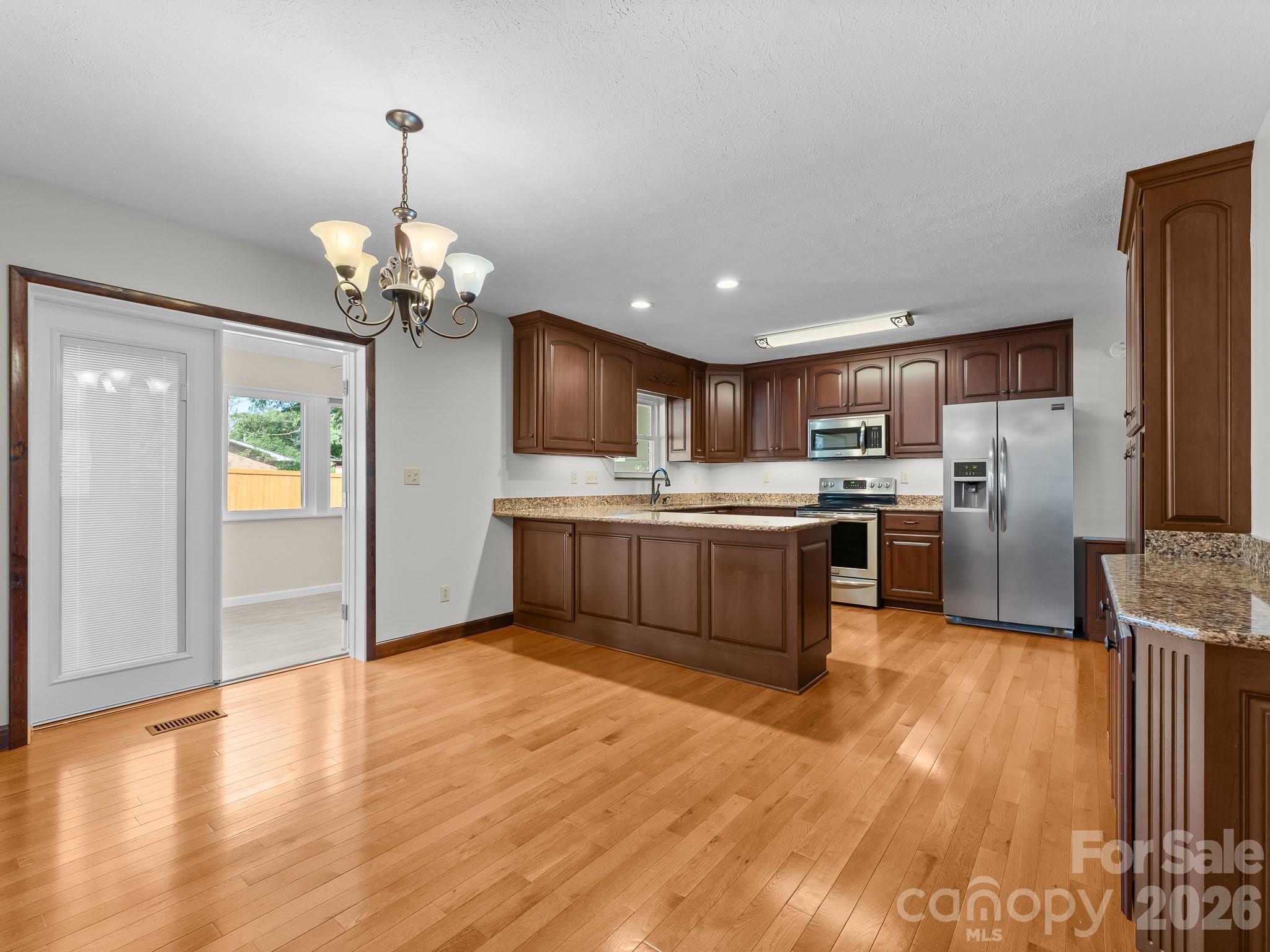 Kitchen with dark wood cabinets, granite island, stainless steel appliances, and hardwood floors.