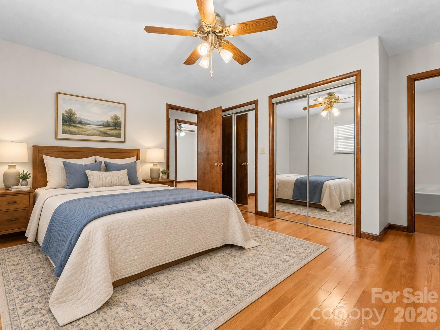 Bedroom with a large white-and-blue bed, mirrored closet doors, and warm wood trim.