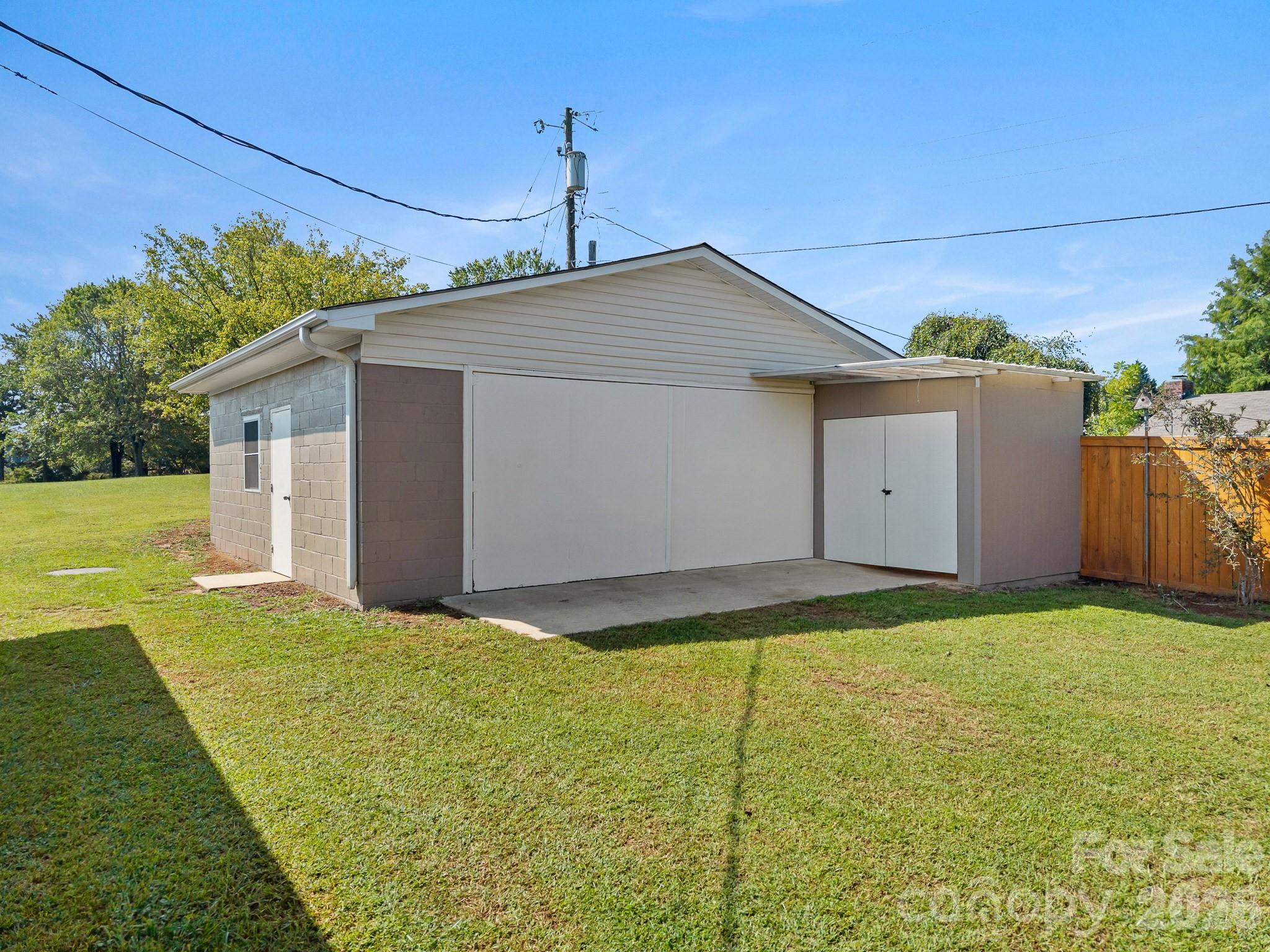 Detached garage with wide white doors, a side entrance, and a grassy lawn.