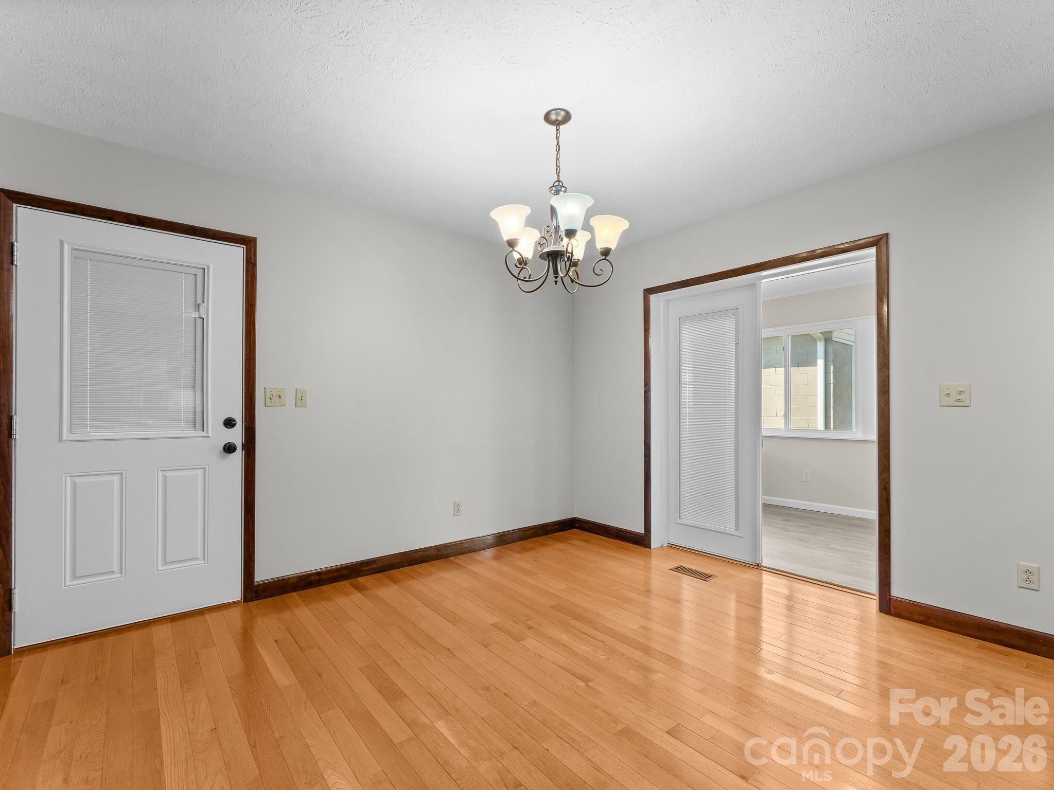 Empty room with hardwood floors, a chandelier, and a white exterior door.