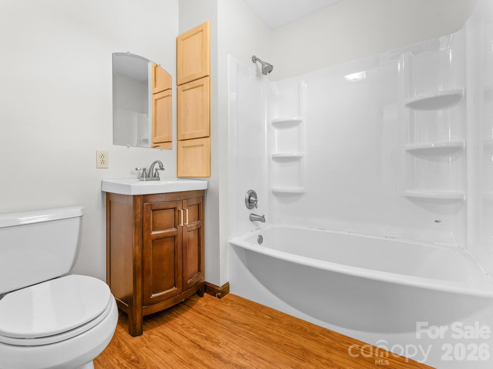 Bathroom with a white tub-shower, dark wood vanity, and wood-look flooring.