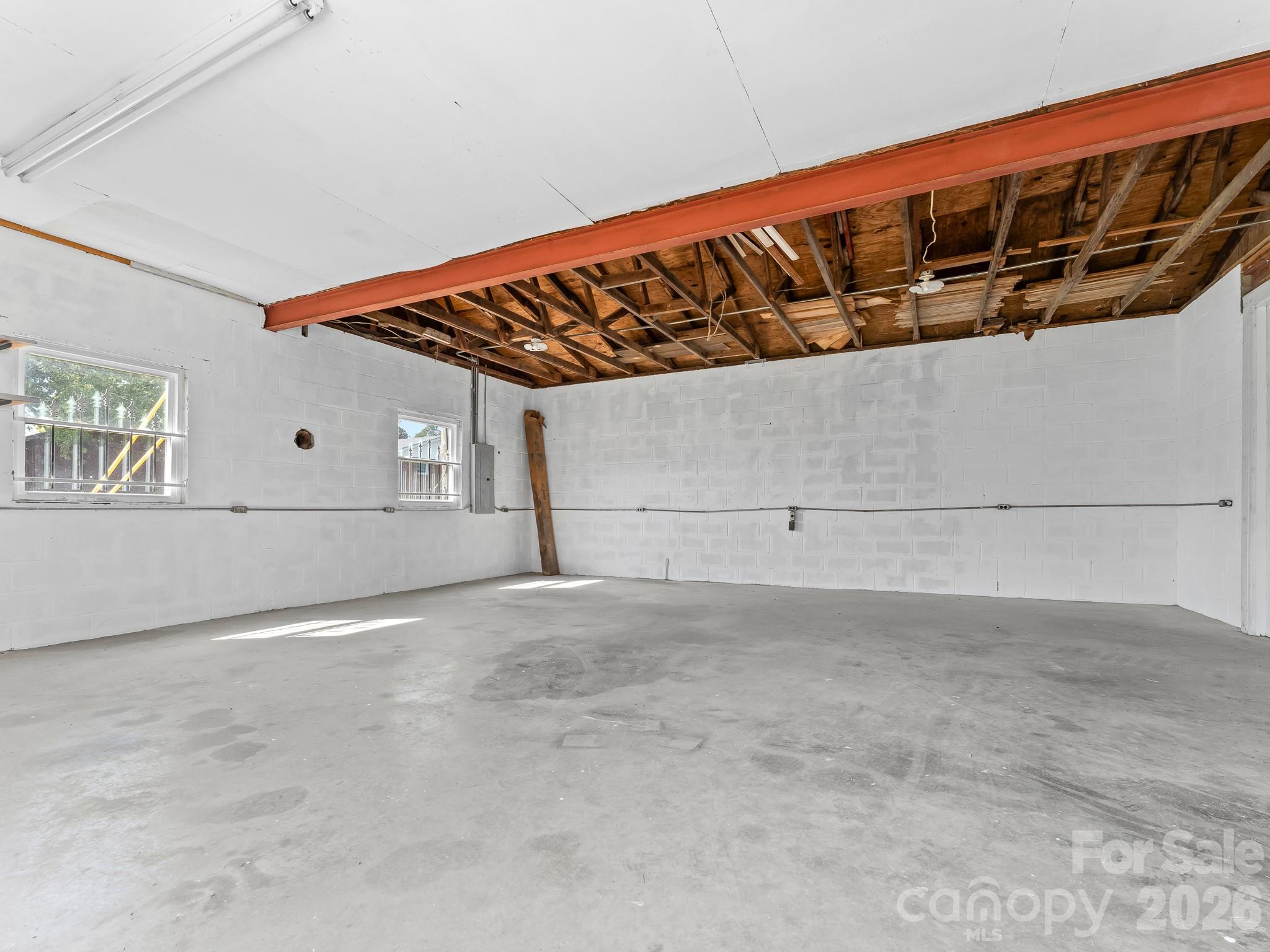Vacant garage with a concrete floor, white block walls, and exposed ceiling framing.