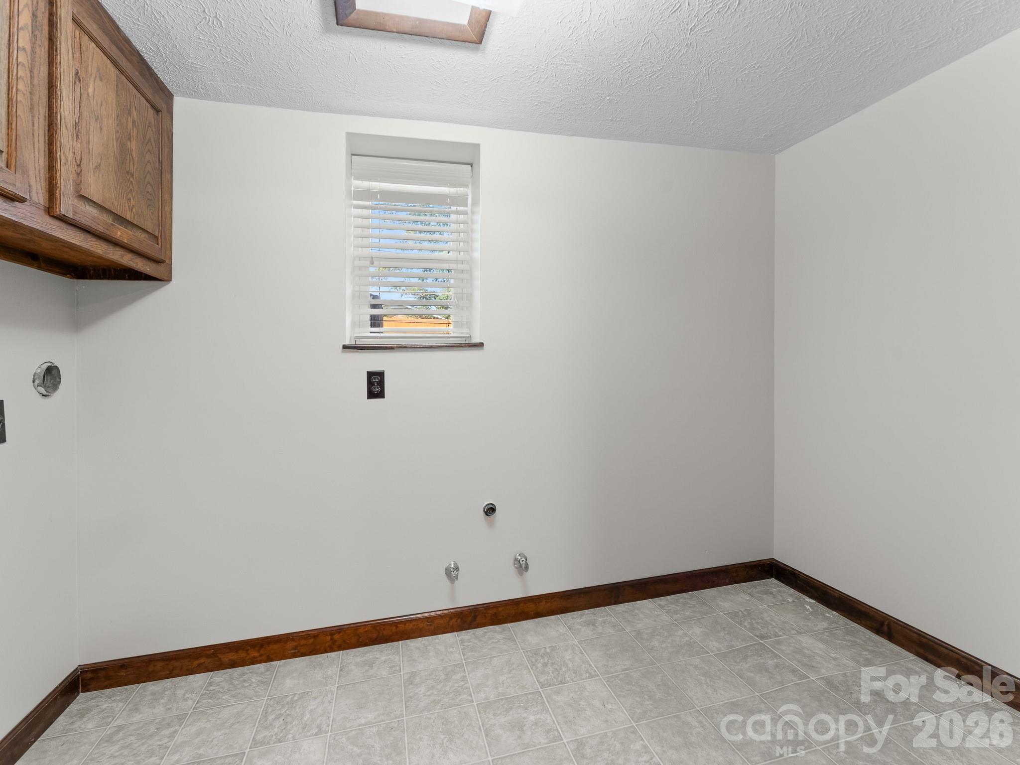 Laundry room with gray tile flooring, dark wood cabinetry, and exposed washer and dryer hookups.