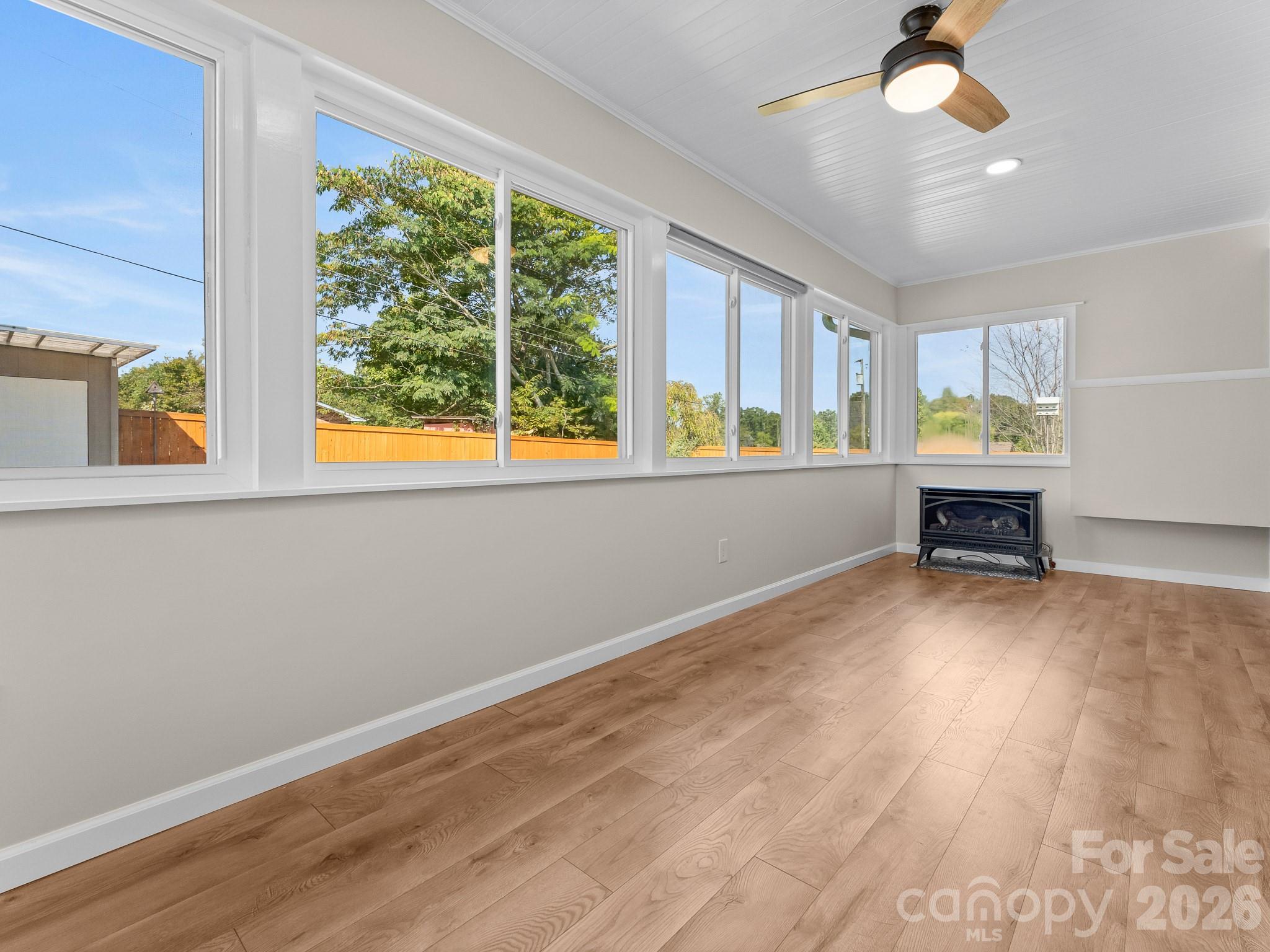 Unfurnished sunroom with wood floors, expansive windows, a ceiling fan, and a freestanding stove.
