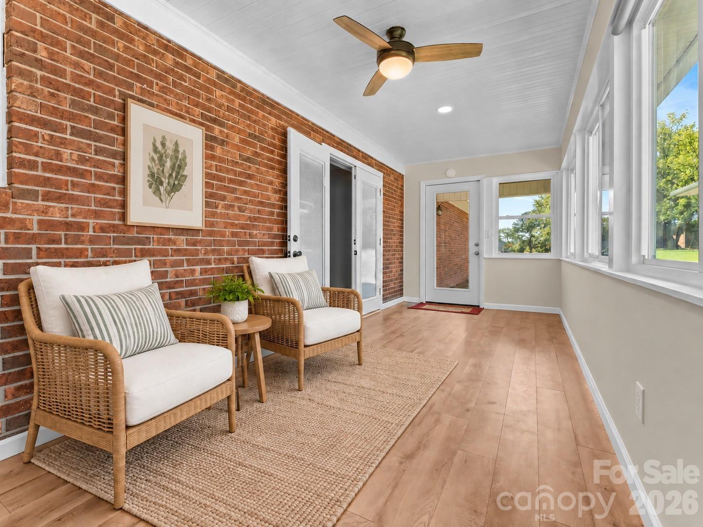 Furnished sunroom with a red brick wall, wicker seating, and large windows overlooking greenery.