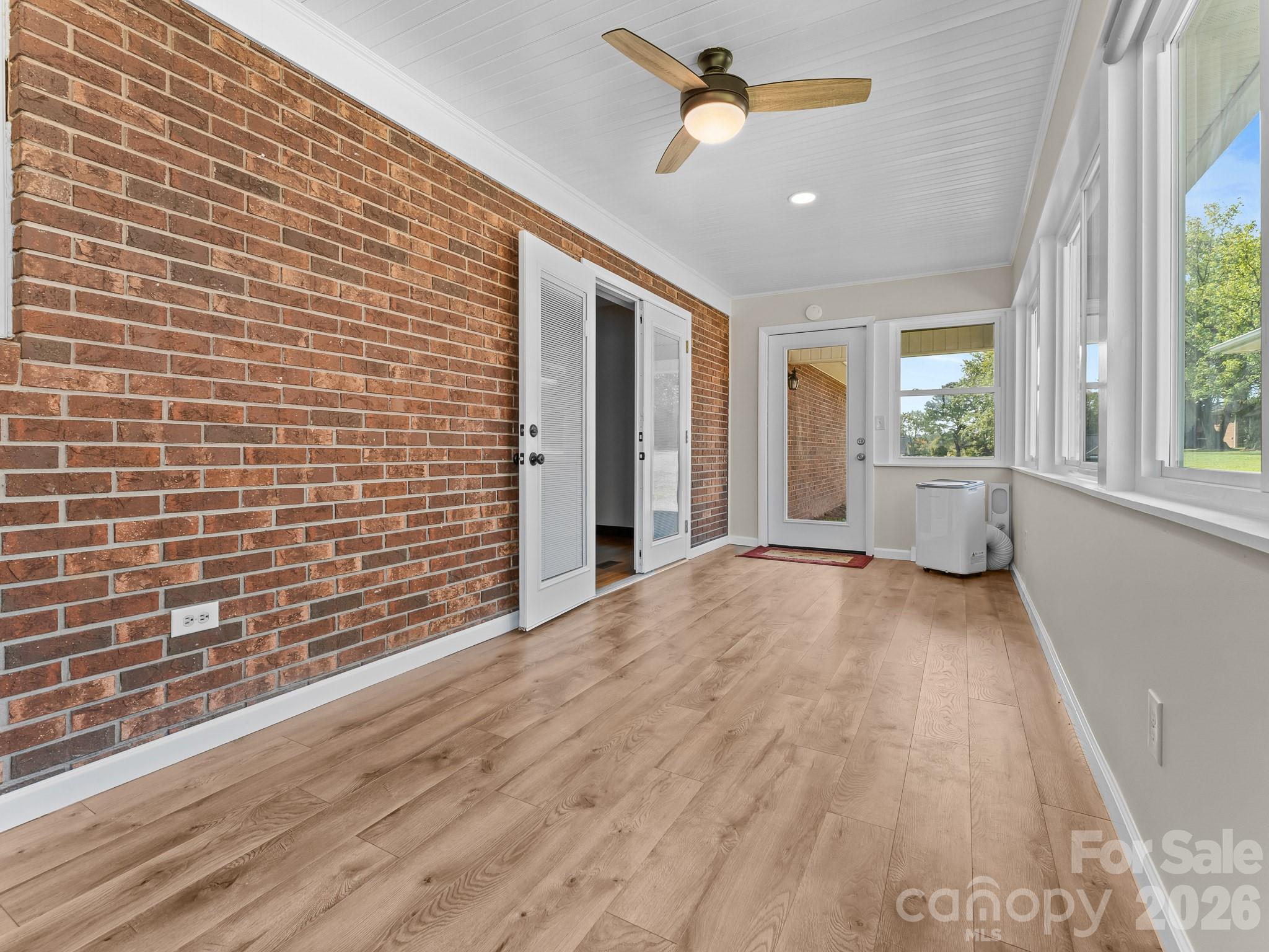 Sunroom with a brick wall, wood flooring, large windows, and a ceiling fan.