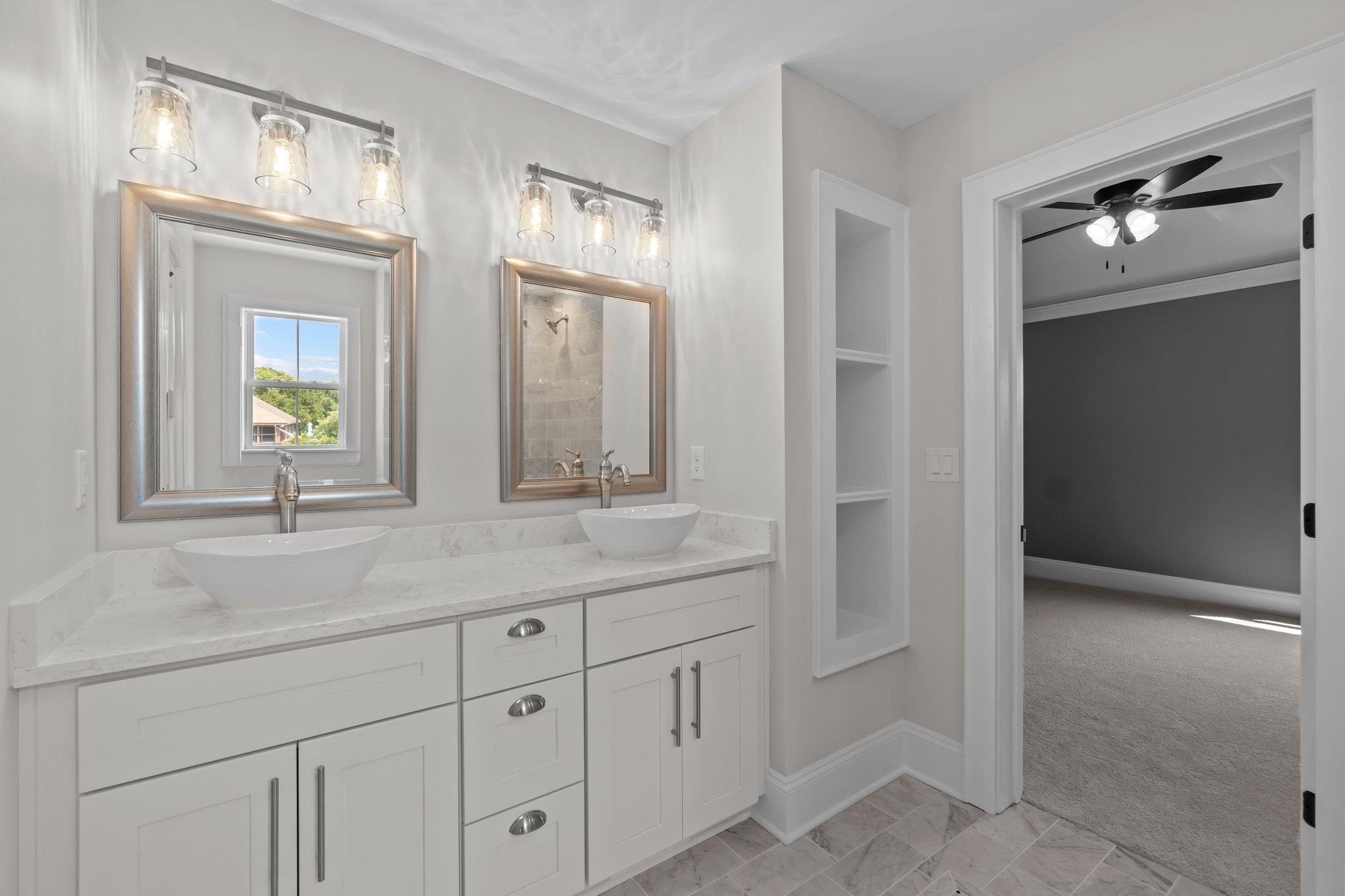 Bathroom with double vessel sinks and a white vanity; doorway opens to a carpeted room.