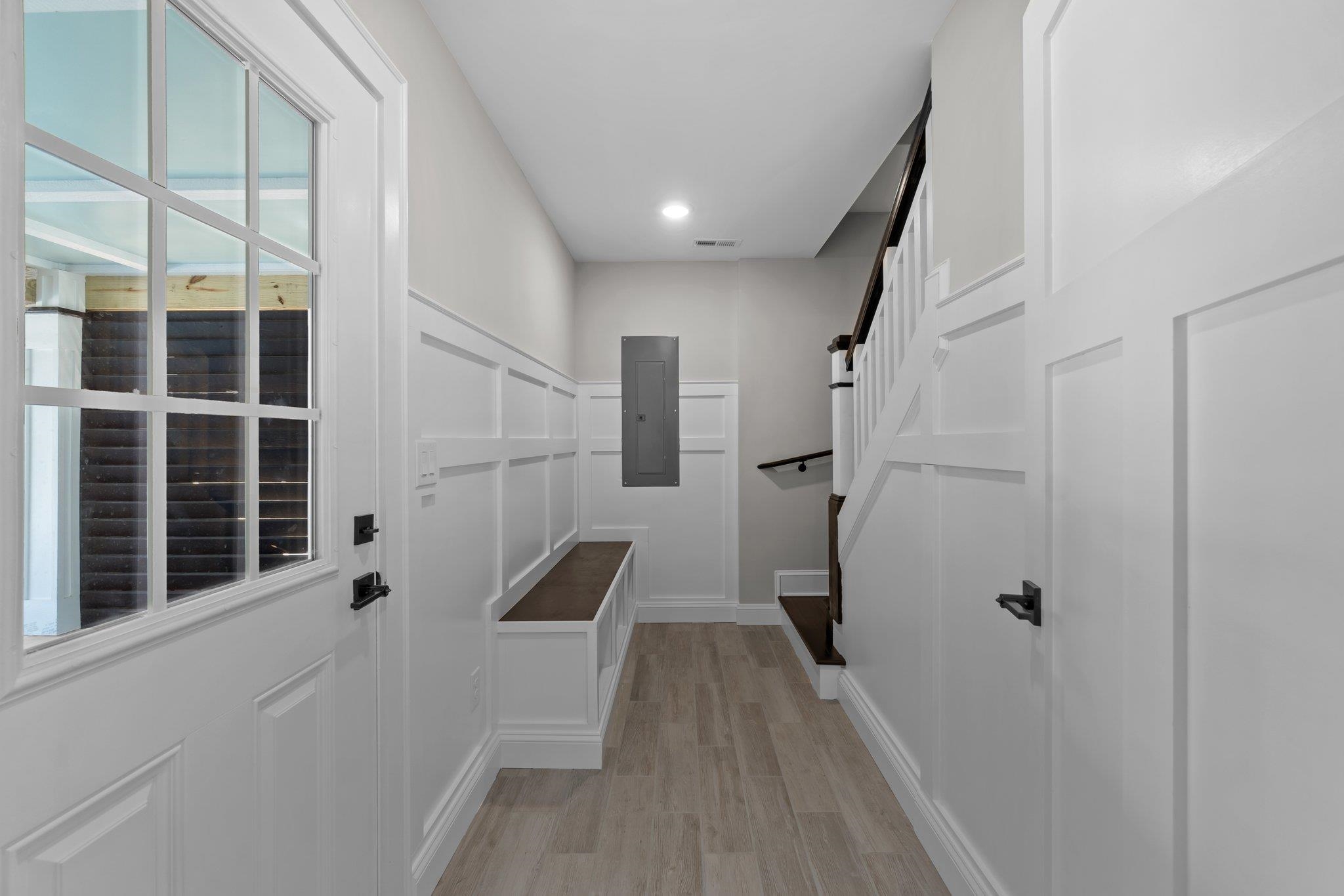 Entry hall with a built-in bench, white paneled walls, and staircase with dark handrails.