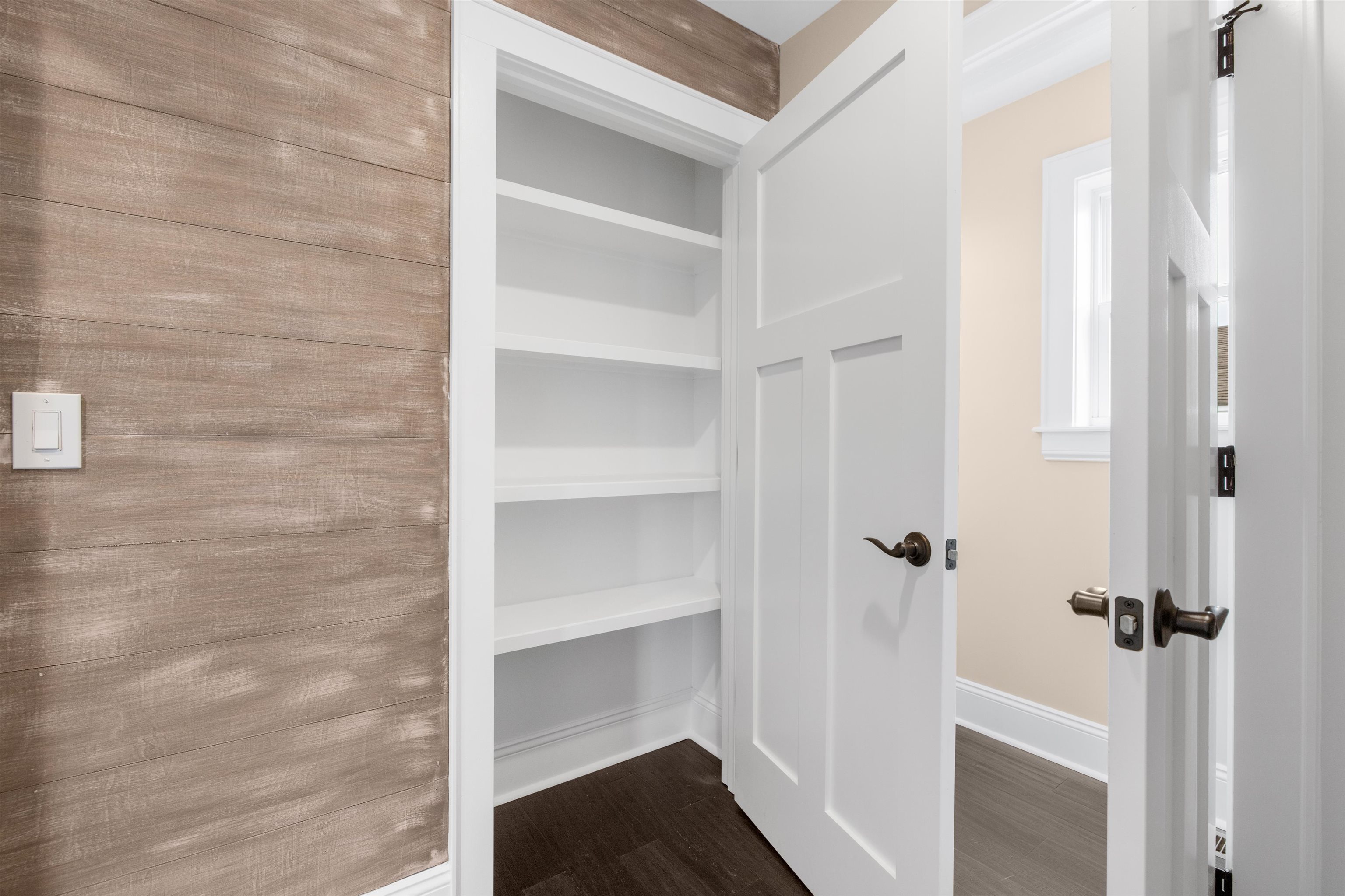 Built-in closet with white shelves beside an open paneled door and wood-look accent wall.