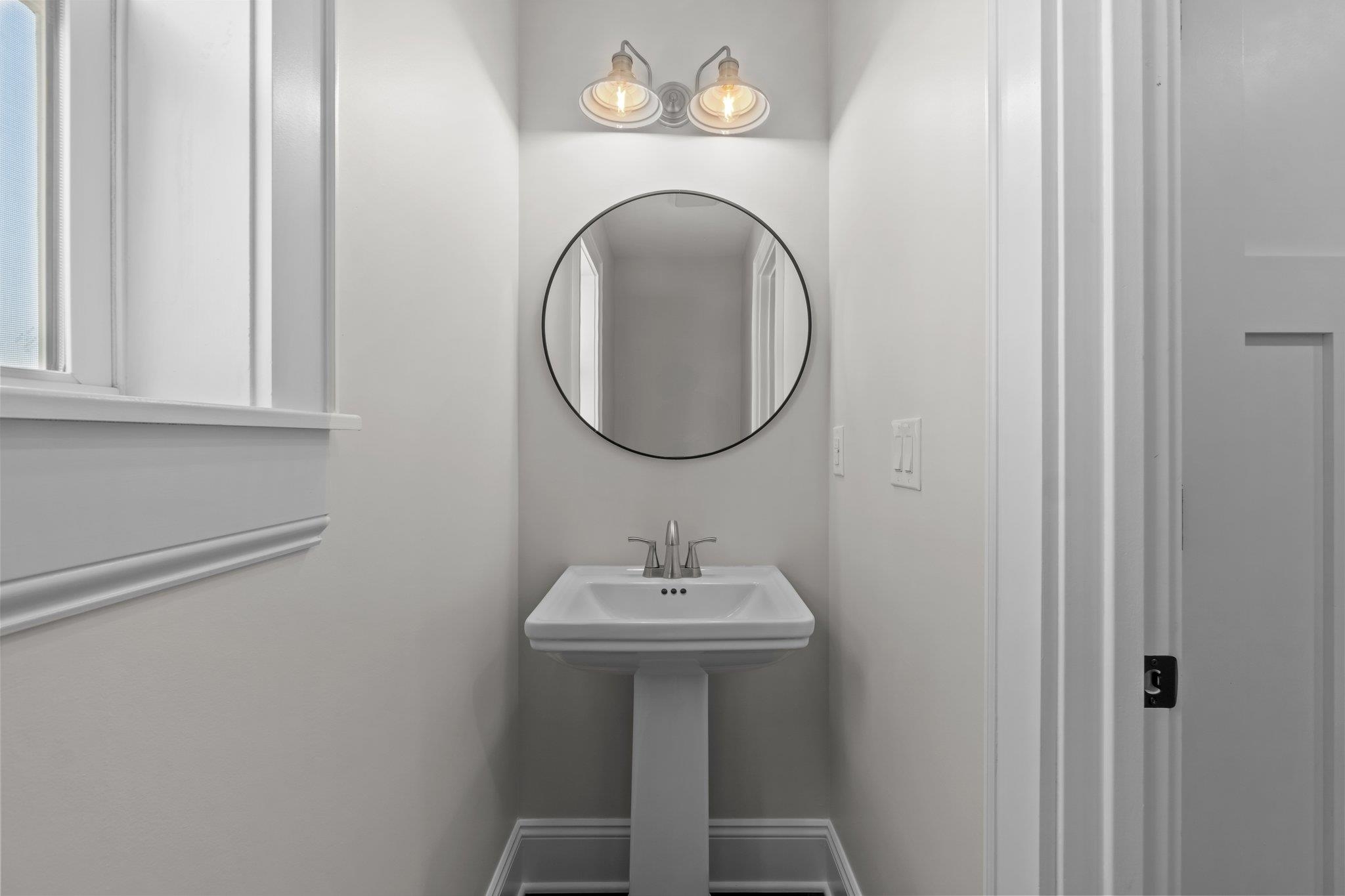 Powder room with a pedestal sink beneath a round mirror and two-light fixture.