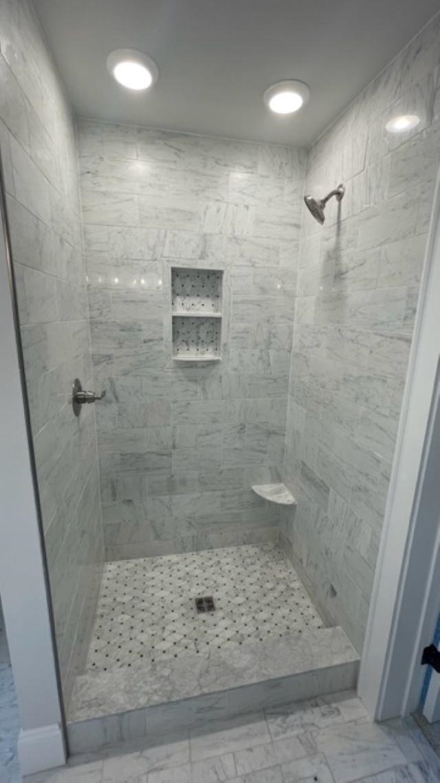 Marble walk-in shower with a recessed niche, corner bench, and mosaic tile floor.