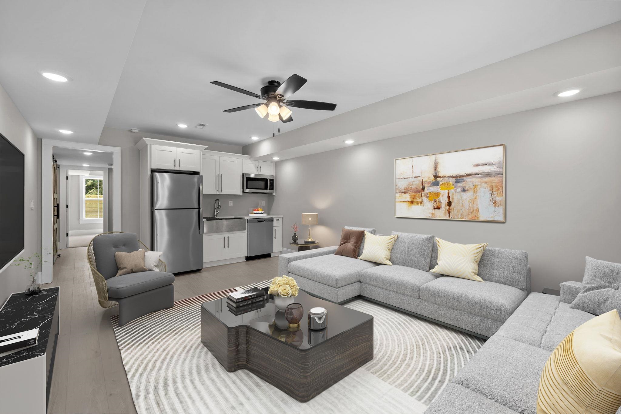 Open-plan living room and kitchen with gray sectional sofas, white cabinets, and stainless steel appliances.