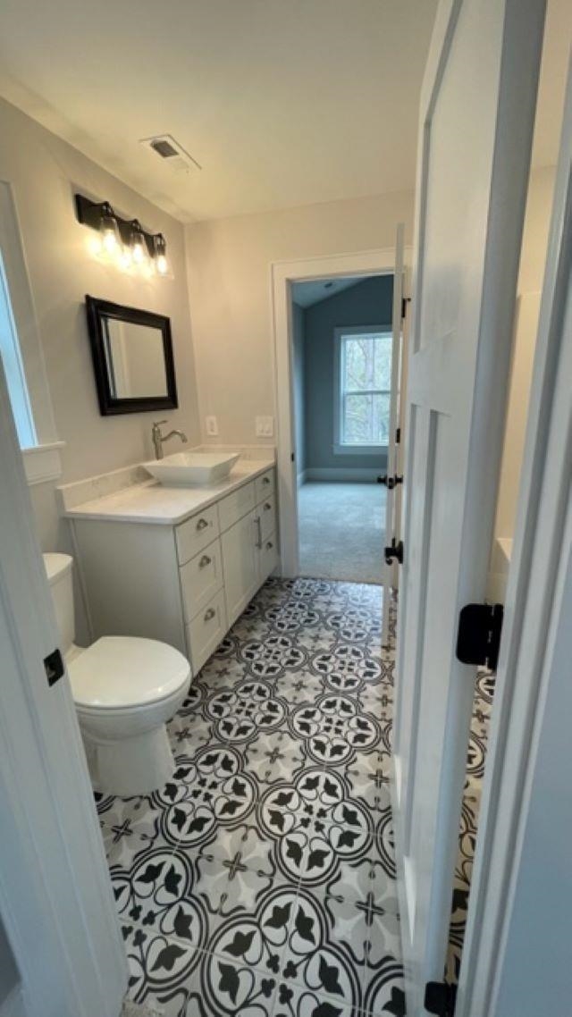 Bathroom with a white vanity and toilet, black-framed mirror, and black-and-white patterned floor tile.