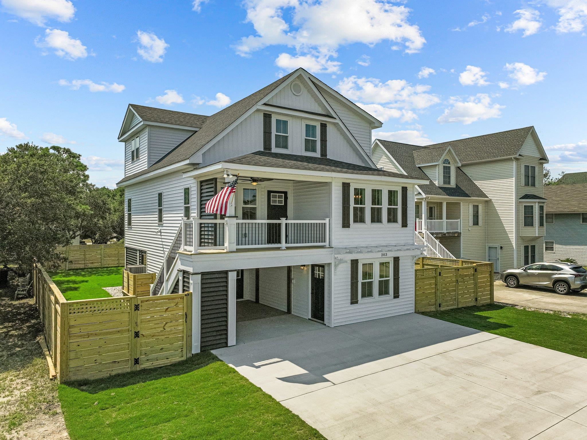 White two-story house with a covered porch, American flag, fenced yard, and covered parking.