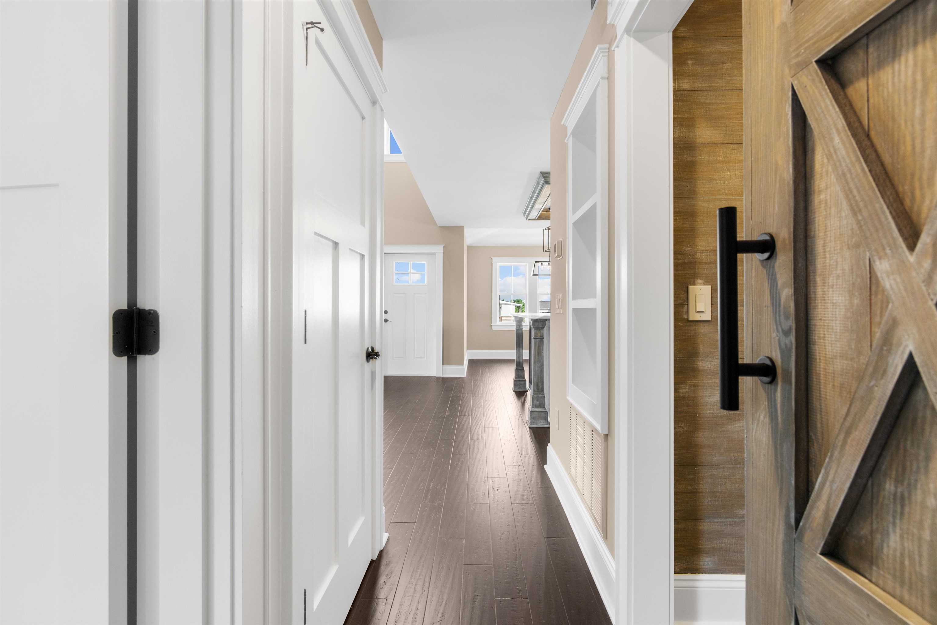 Bright entry hallway with dark wood floors, white doors, and a rustic sliding barn door.