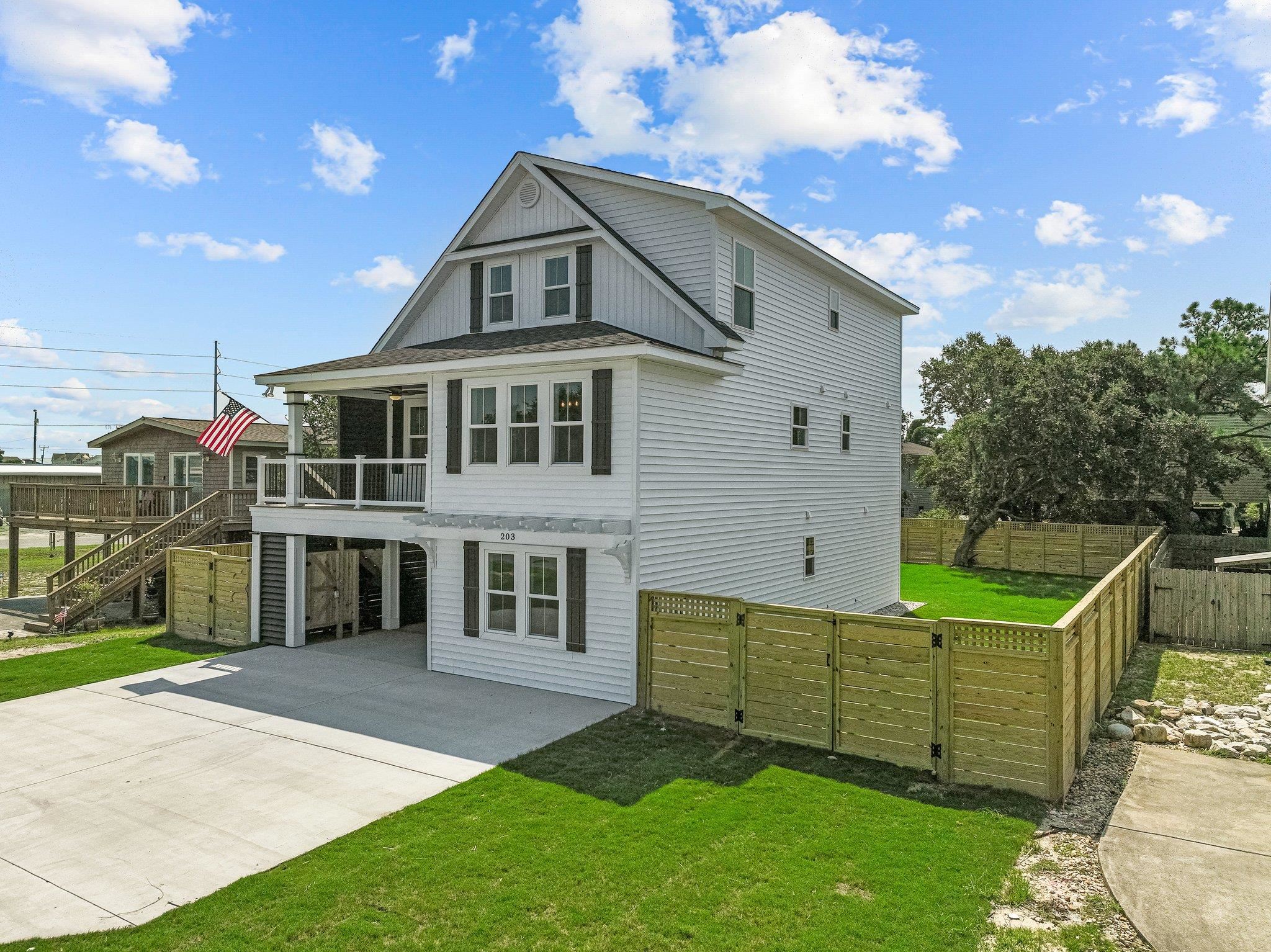 White two-story house with a covered porch, fenced yard, and broad concrete driveway.