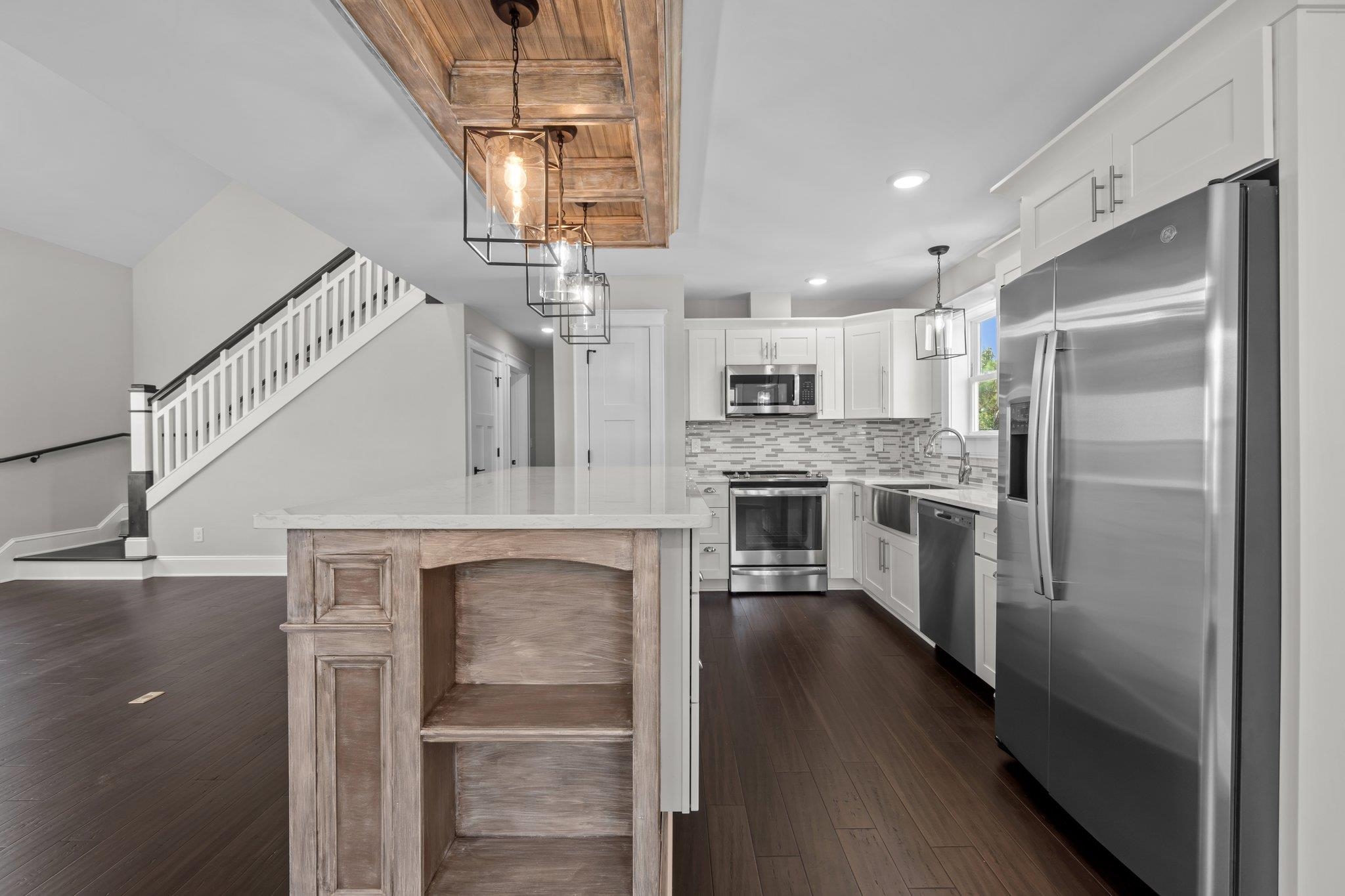 Kitchen with white cabinets, stainless steel appliances, a large wood-base island, and an adjacent staircase.