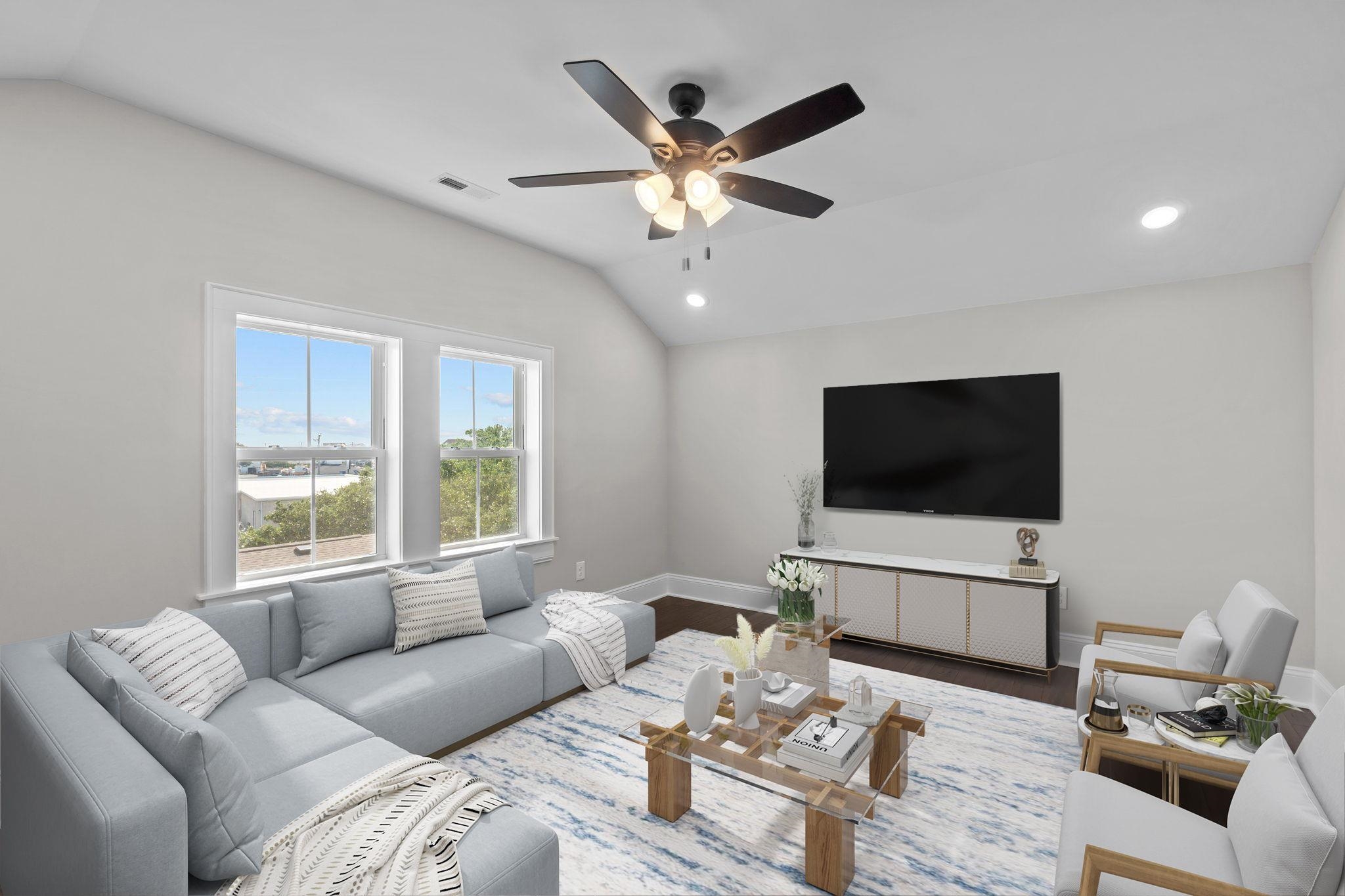 Furnished living room with vaulted ceiling, gray sectional, two large windows, and wall-mounted television.