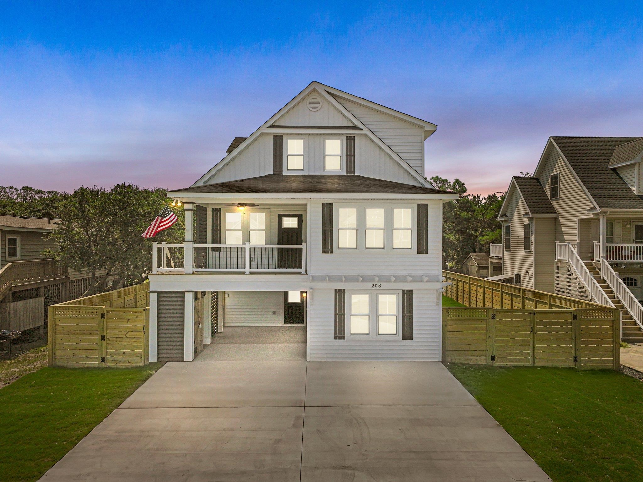 White two-story home with a covered porch, fenced yard, and wide driveway at dusk.