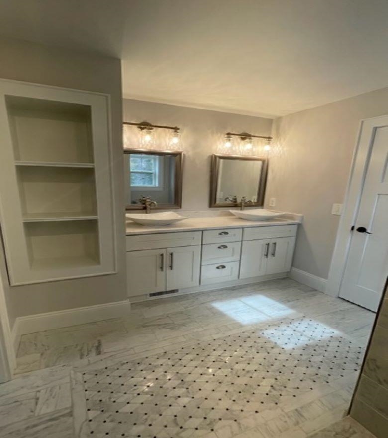 Bathroom with a double-sink vanity, two framed mirrors, and a marble floor with a patterned tile inset.