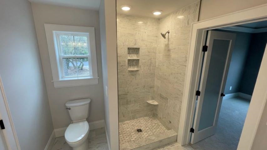 Bathroom with marble-look walk-in shower, built-in niches, corner seat, and toilet beneath a window.