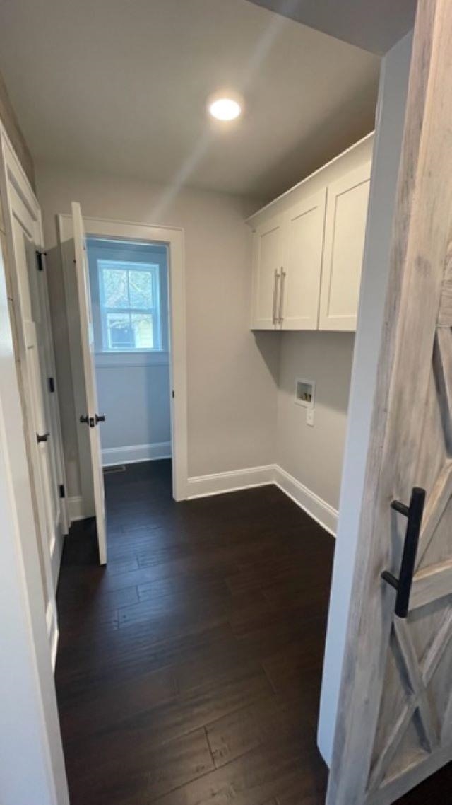 Laundry room with white cabinets, utility connections, dark flooring, and a sliding barn-style door.