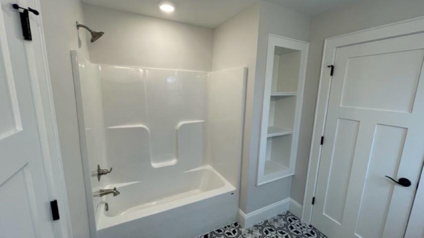 Bathroom with a white tub and shower, built-in shelves, and patterned black-and-white floor tile.